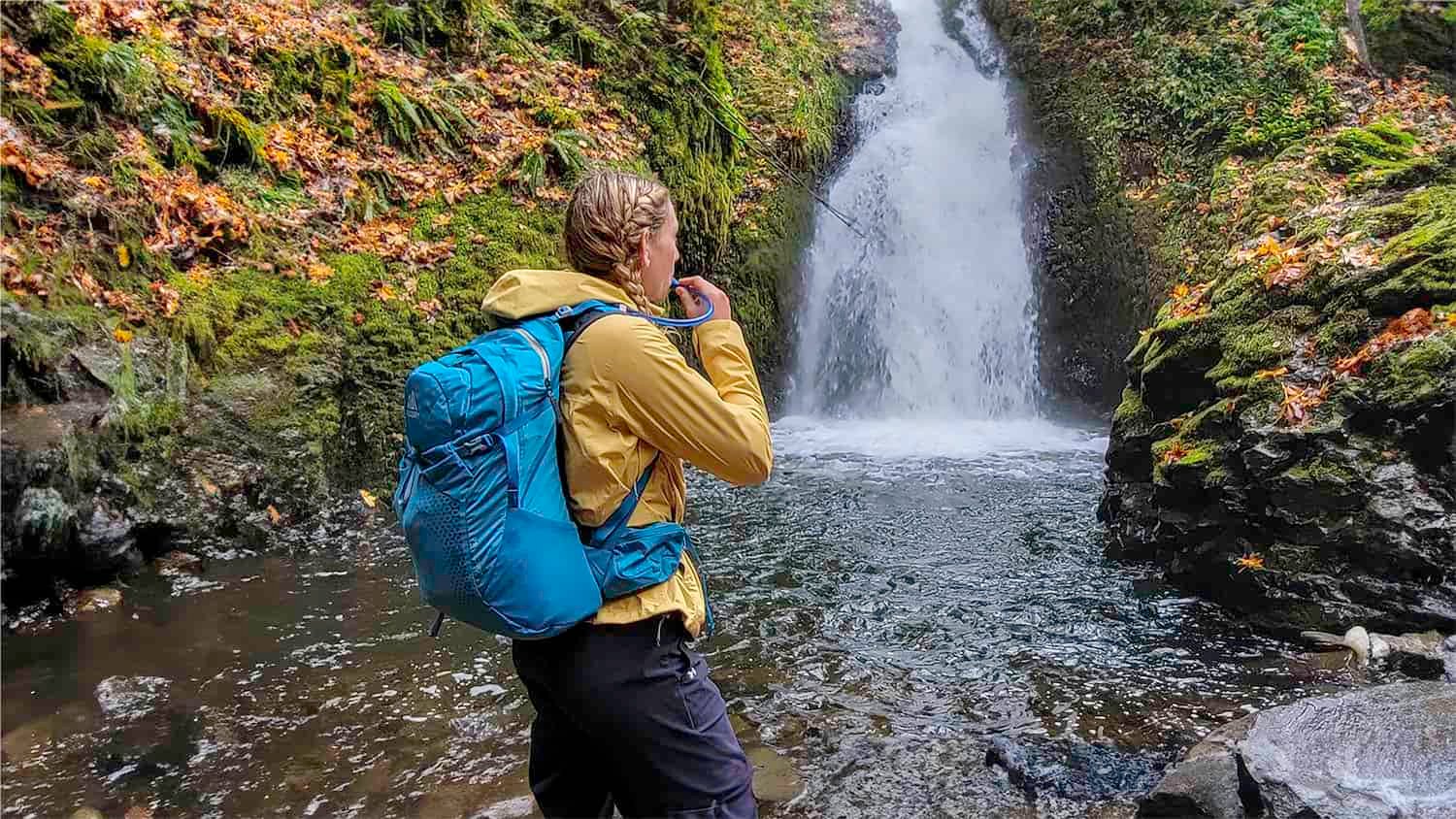 A hiker in front of a waterfall with the Gregory Juno 24 H2O hydration pack