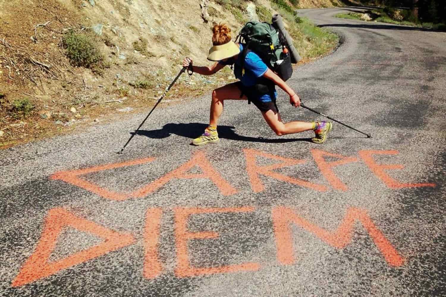 A female hiker strikes a pose on a road spray painted with the words "carpe diem" (seize the day)