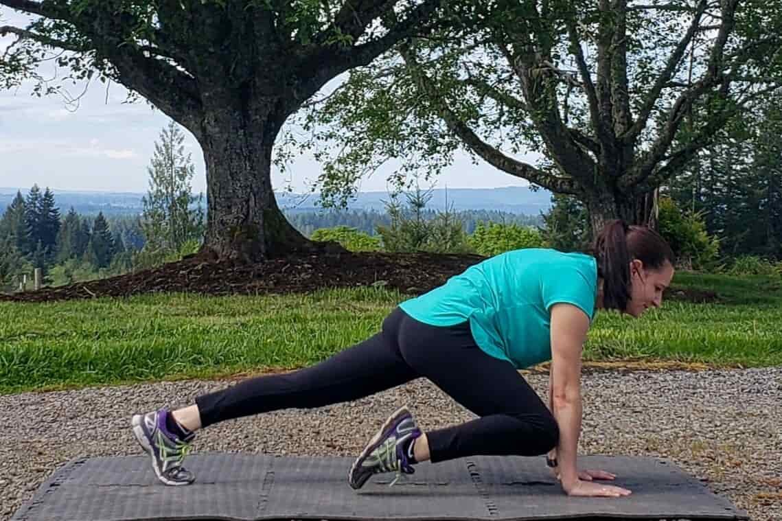 A woman does mountain climbers in a parking lot on a mat 