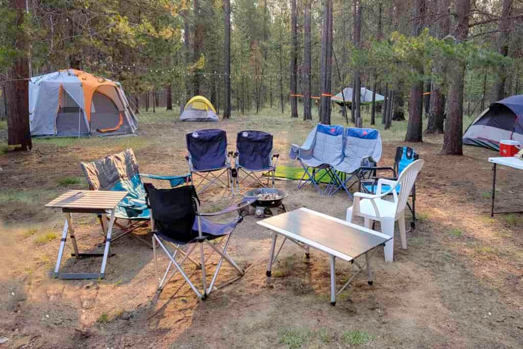Camping chairs circled around a propane campfire with tents in the background