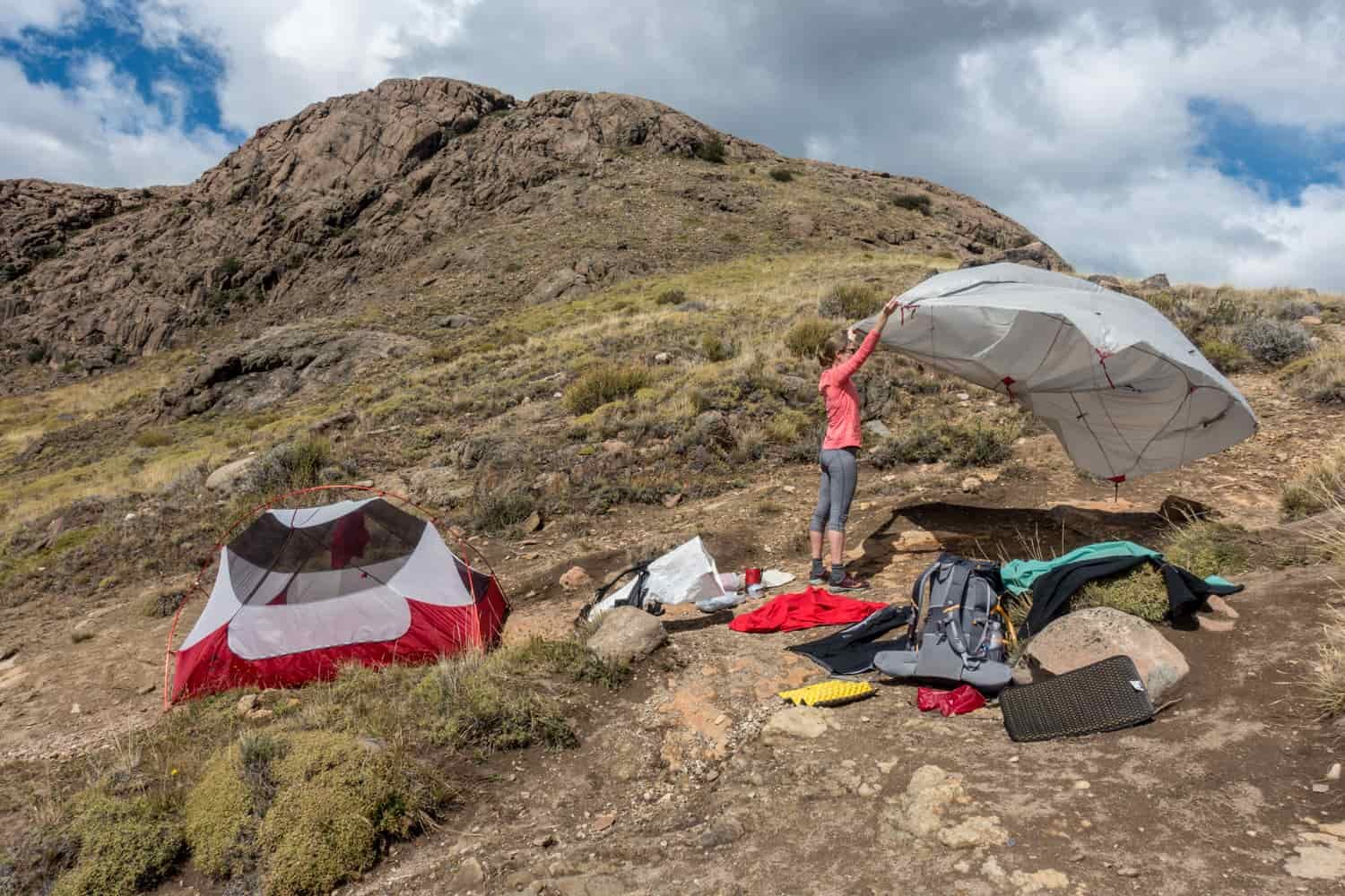 A female backpacker pitches a tent while setting up camp near a mountain saddle