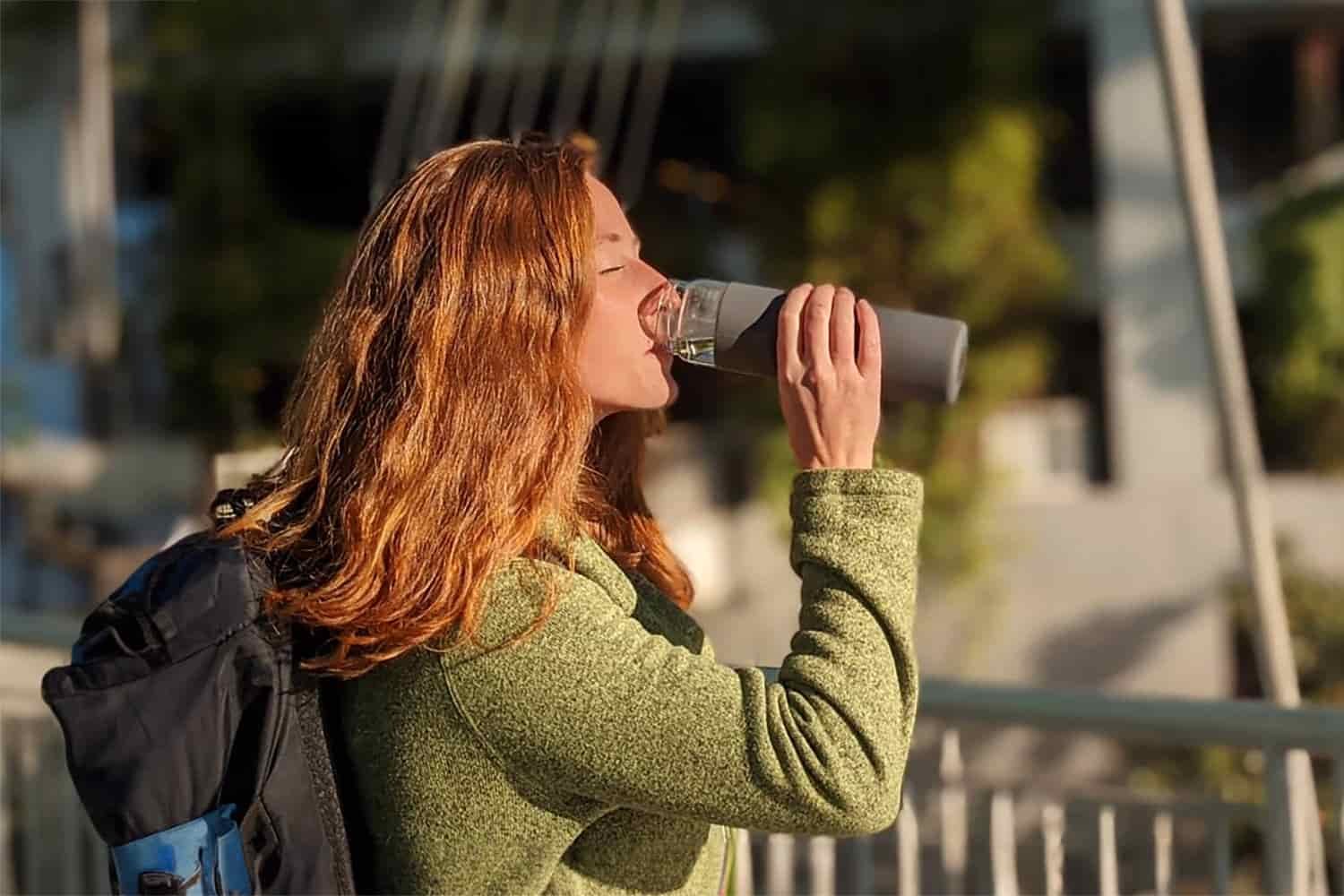 A red-headed woman drinking out of the Yomious 20 oz. water bottle at the airport