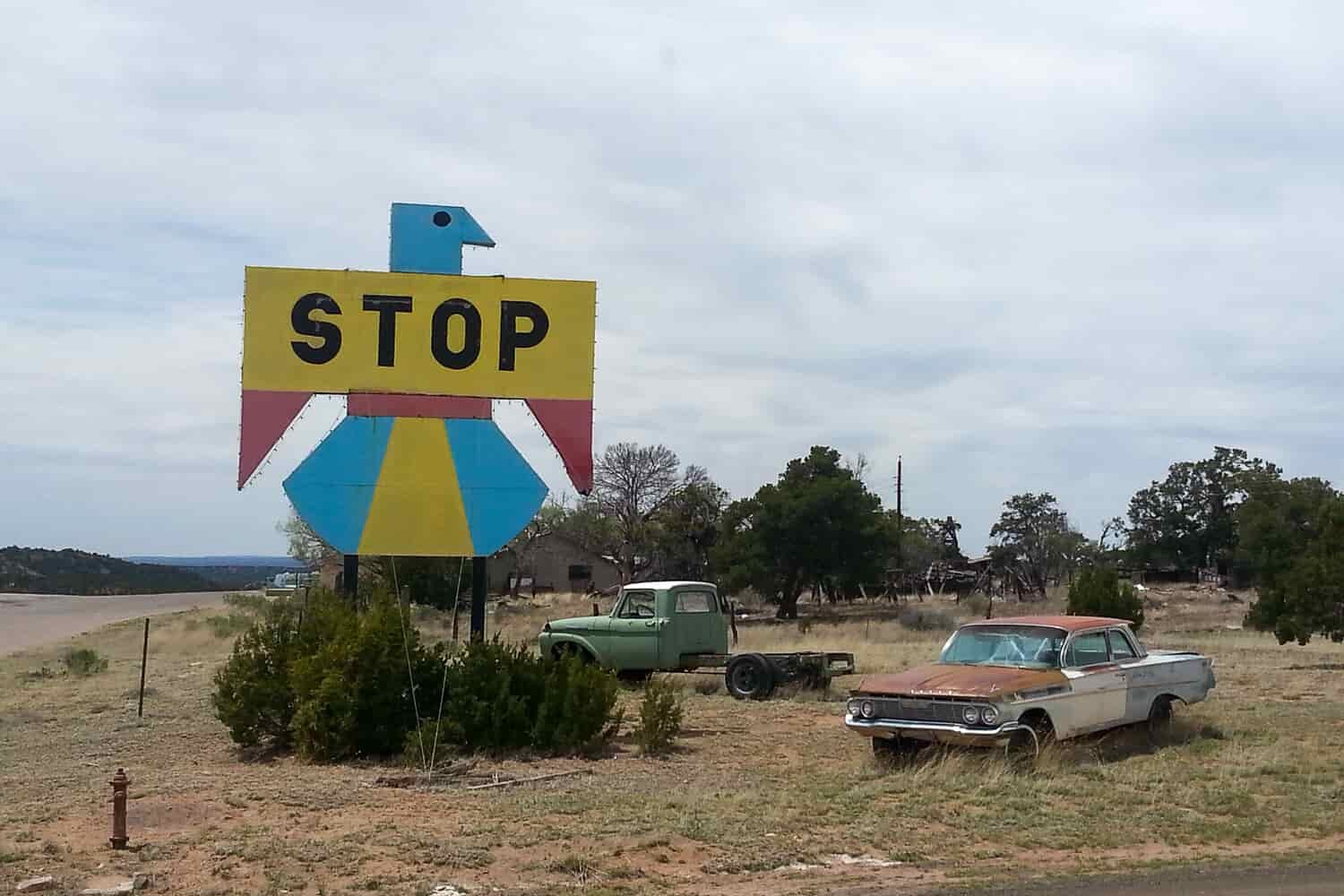 image of broken down, rusty vintage cars and a blue and yellow sign that says, "STOP" in the shape of a bird