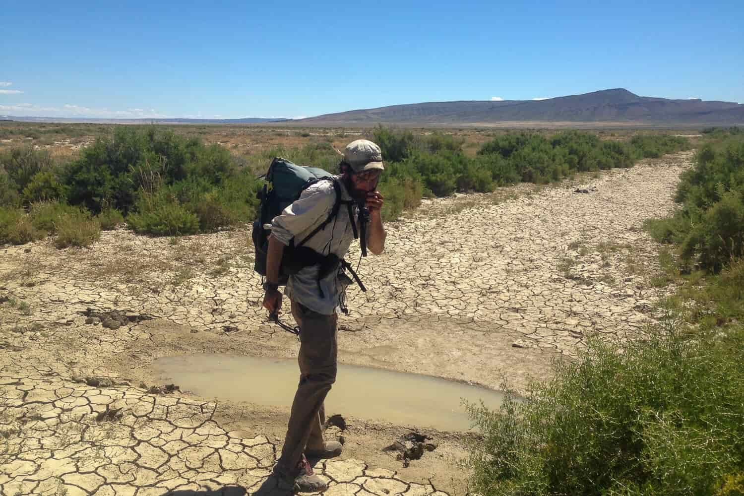Backpacker on the CDT in front of a water source which is a small muddy rut in the desert.
