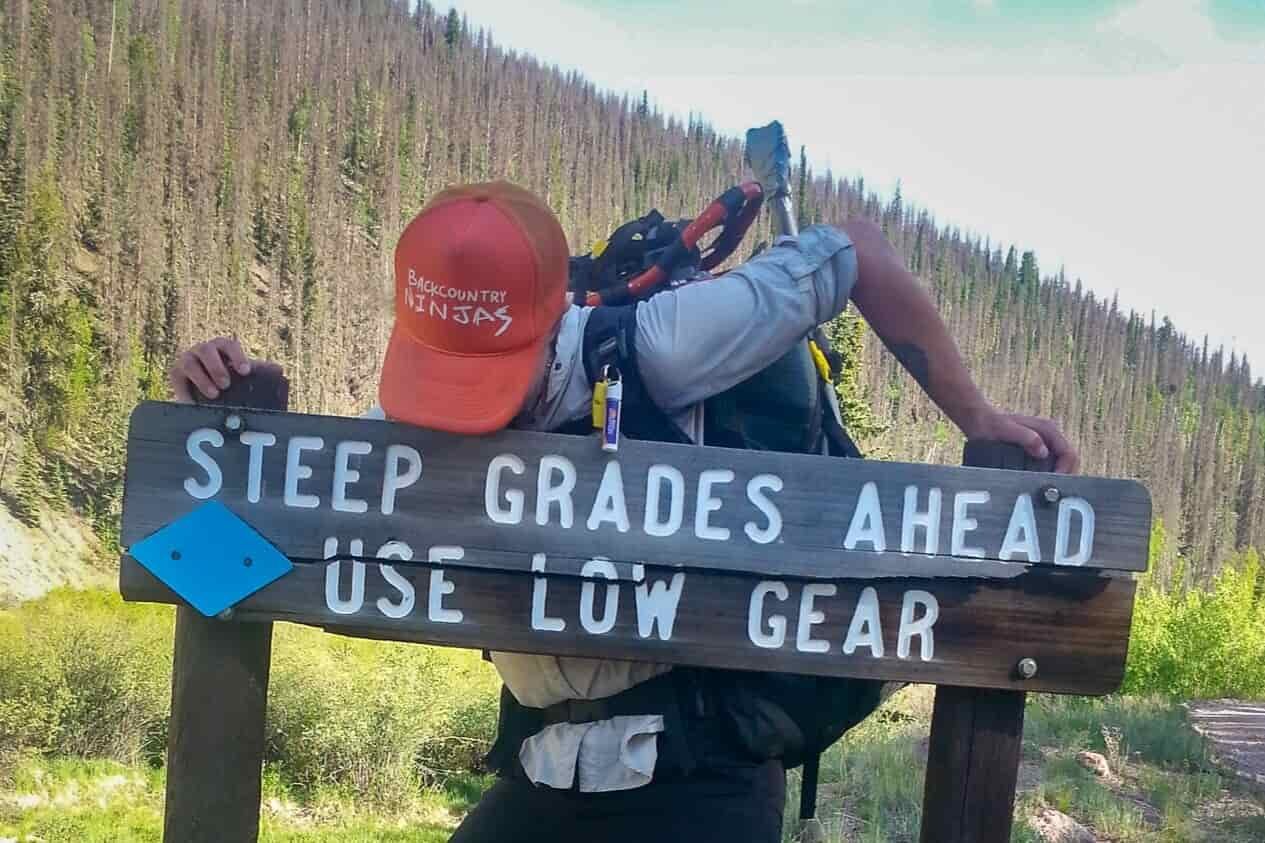 thru-hiker posing in front of a sign that says "steep grades ahead use low gear."