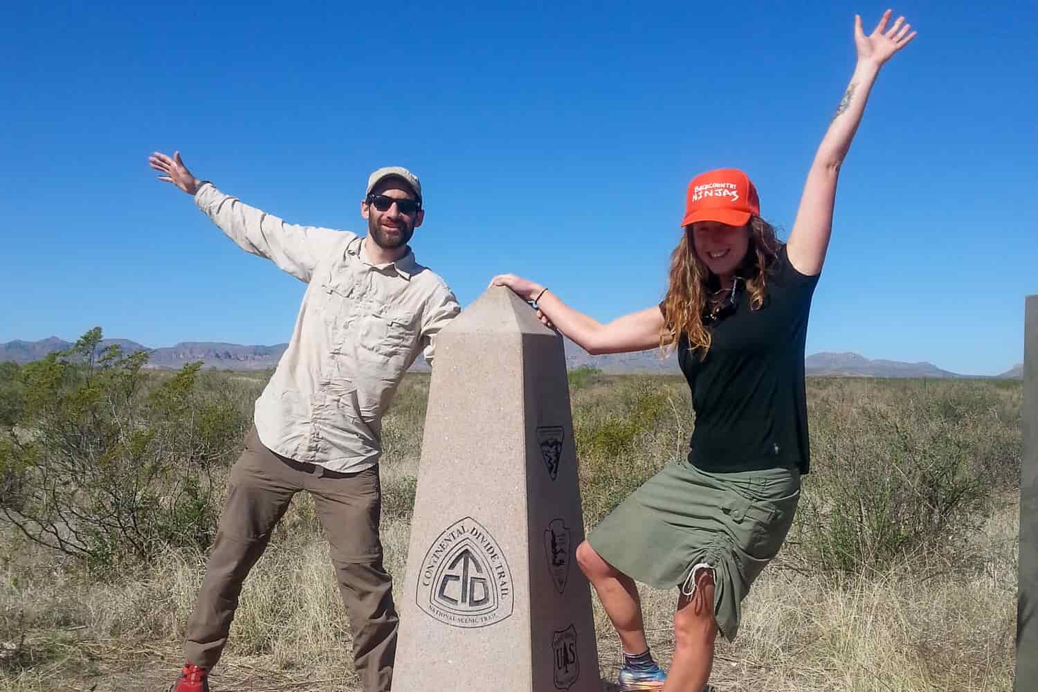 two CDT thru-hikers holding their arms up to pose next to the CDT southern terminus monument.