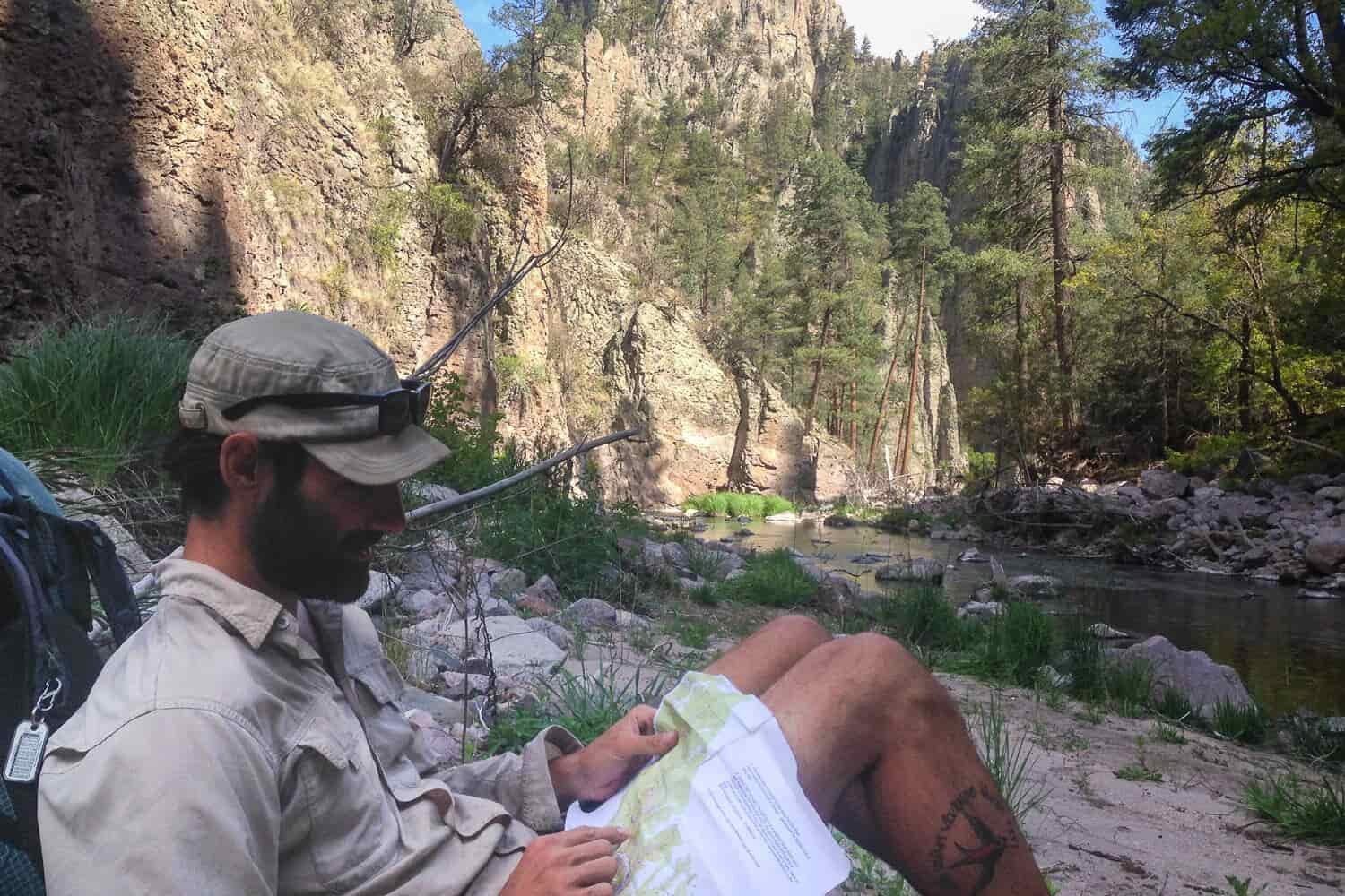 backpacker on the CDT sitting along a river looking a trail map