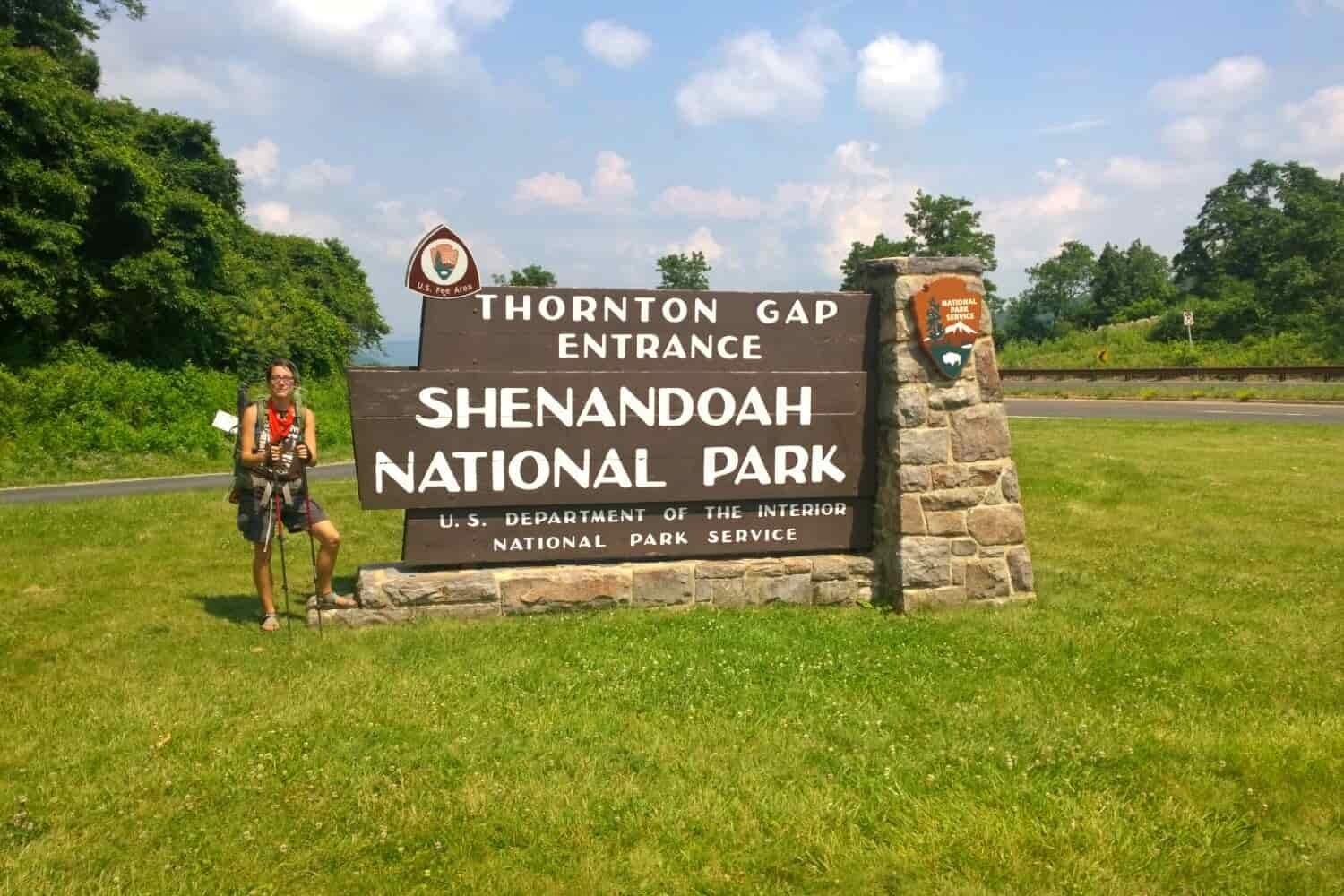 Thru-hiker on the Appalachian Trail posing in front of Shenandoah National Park's entrance sign