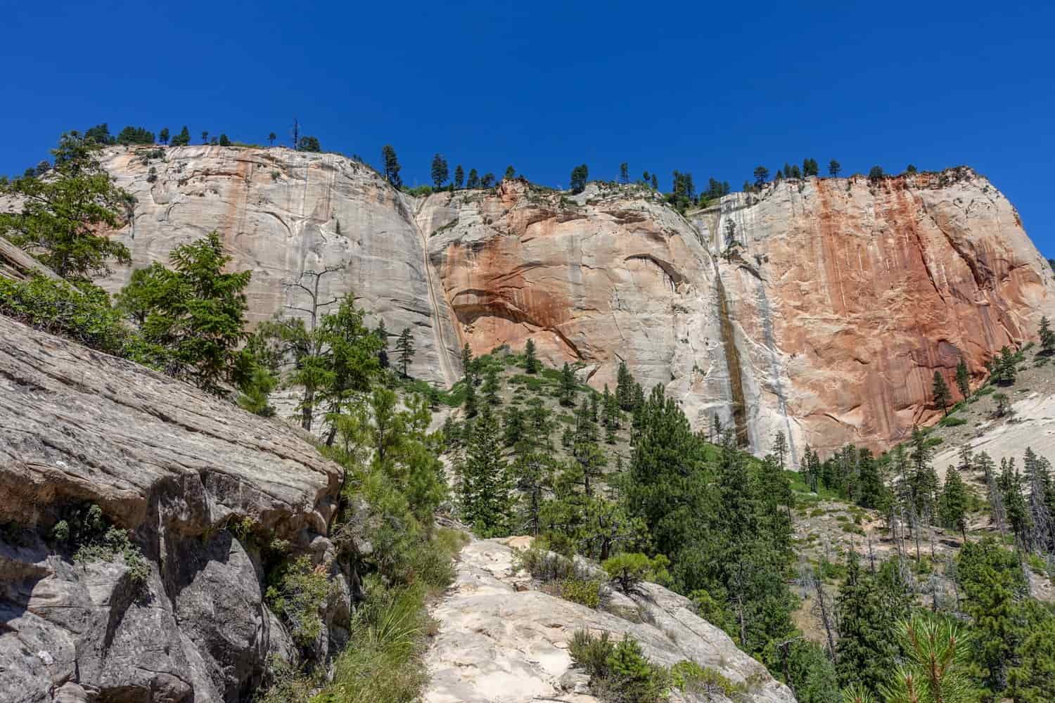 steep walls in white and red with green trees at the base of the rock towers