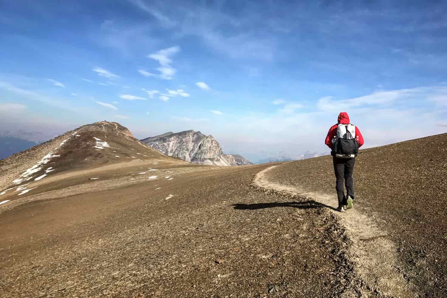 a backpacker on the skyline trail in jasper national park with their hood on while hiking well above tree line with mountains in all directions