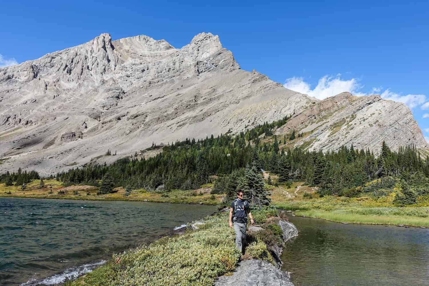 backpacker walking between two lakes with a mountain in the background