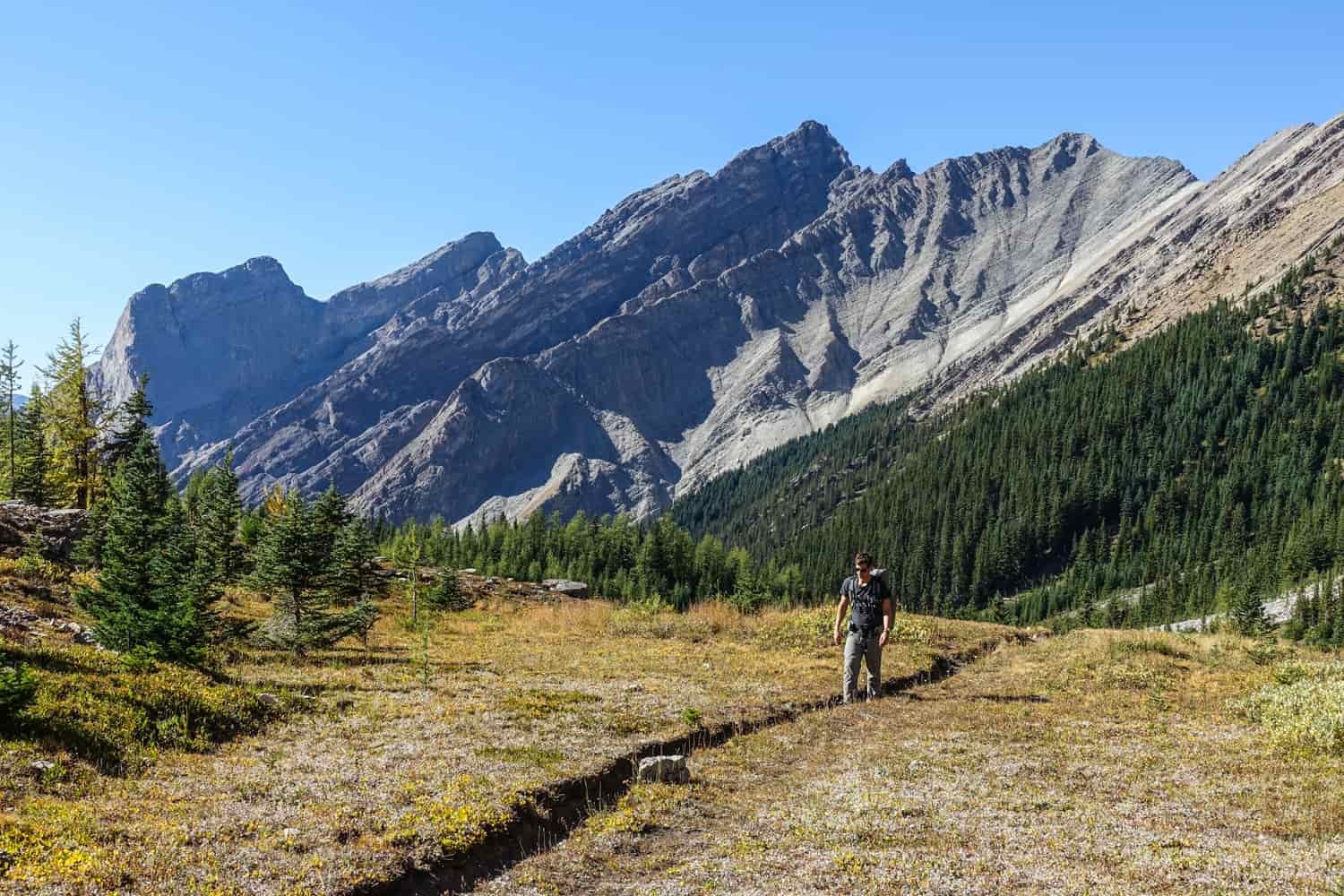 backpacker on a trail below rocky peaks in banff national park