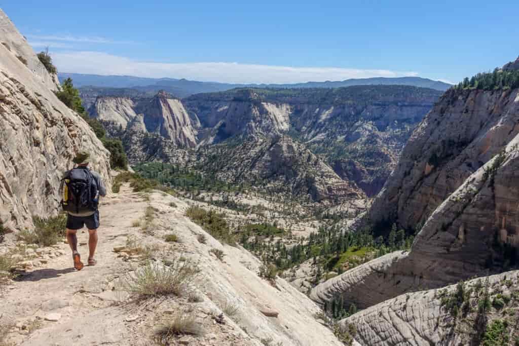 a white/gray rocky section of the zion traverse with a backpacker walking on an exposed trail.
