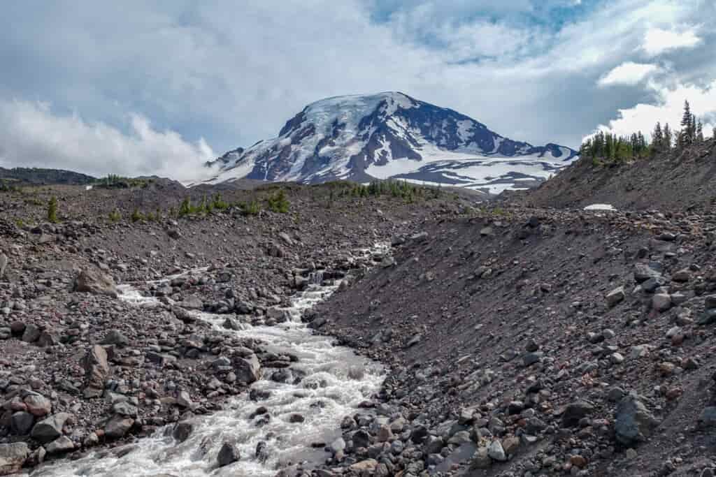 A stream of snowmelt flows down from Mt Adams through a rocky gully 