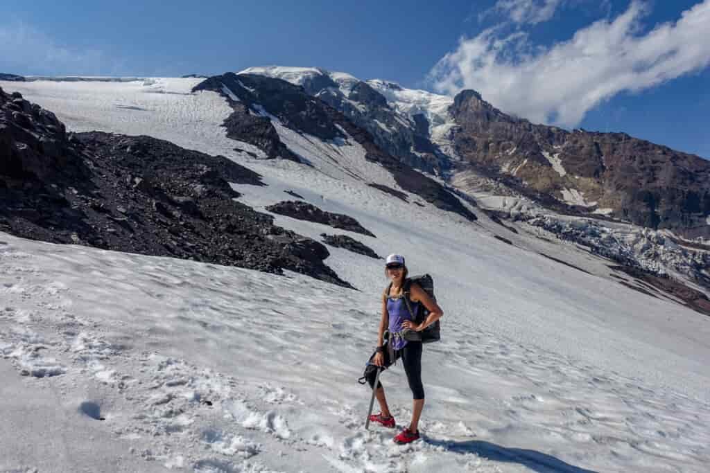 A female backpacker poses on a snowfield while hiking through the Mount Adams wilderness