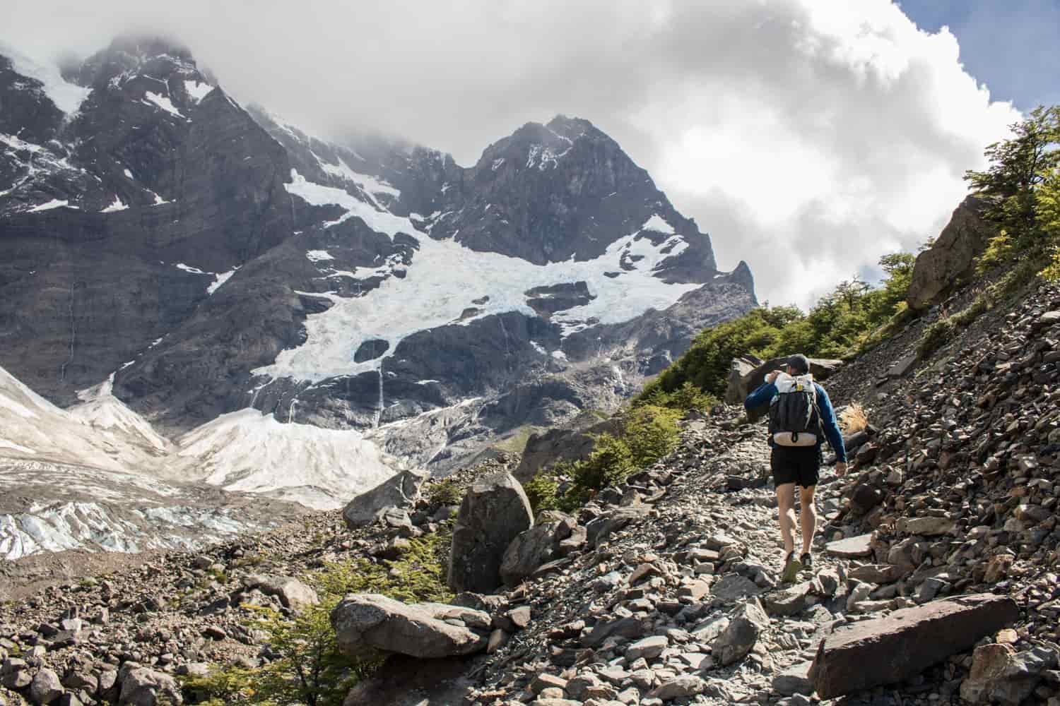 A male hiker makes his way up a steep and rocky trail wearing an ultralight backpack