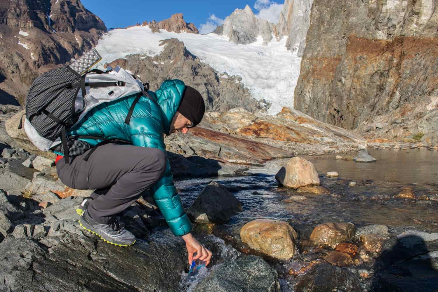A hiker fills his water bottle from a stream flowing out of a glacier
