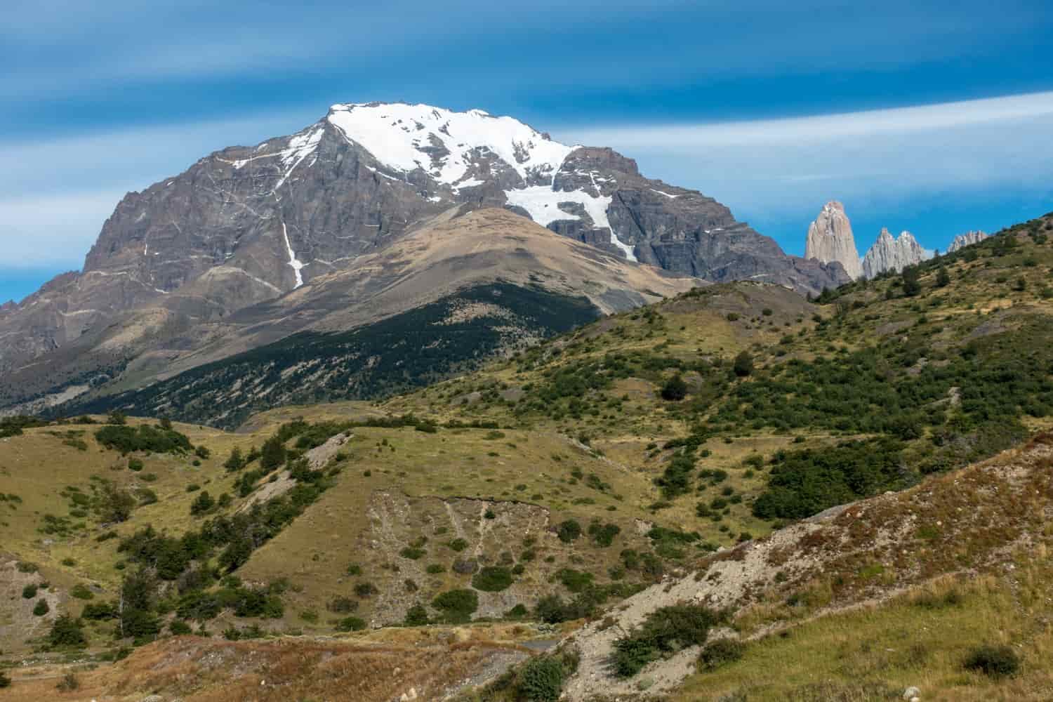 A landscape shot with green grasslands leading up to a rugged mountain