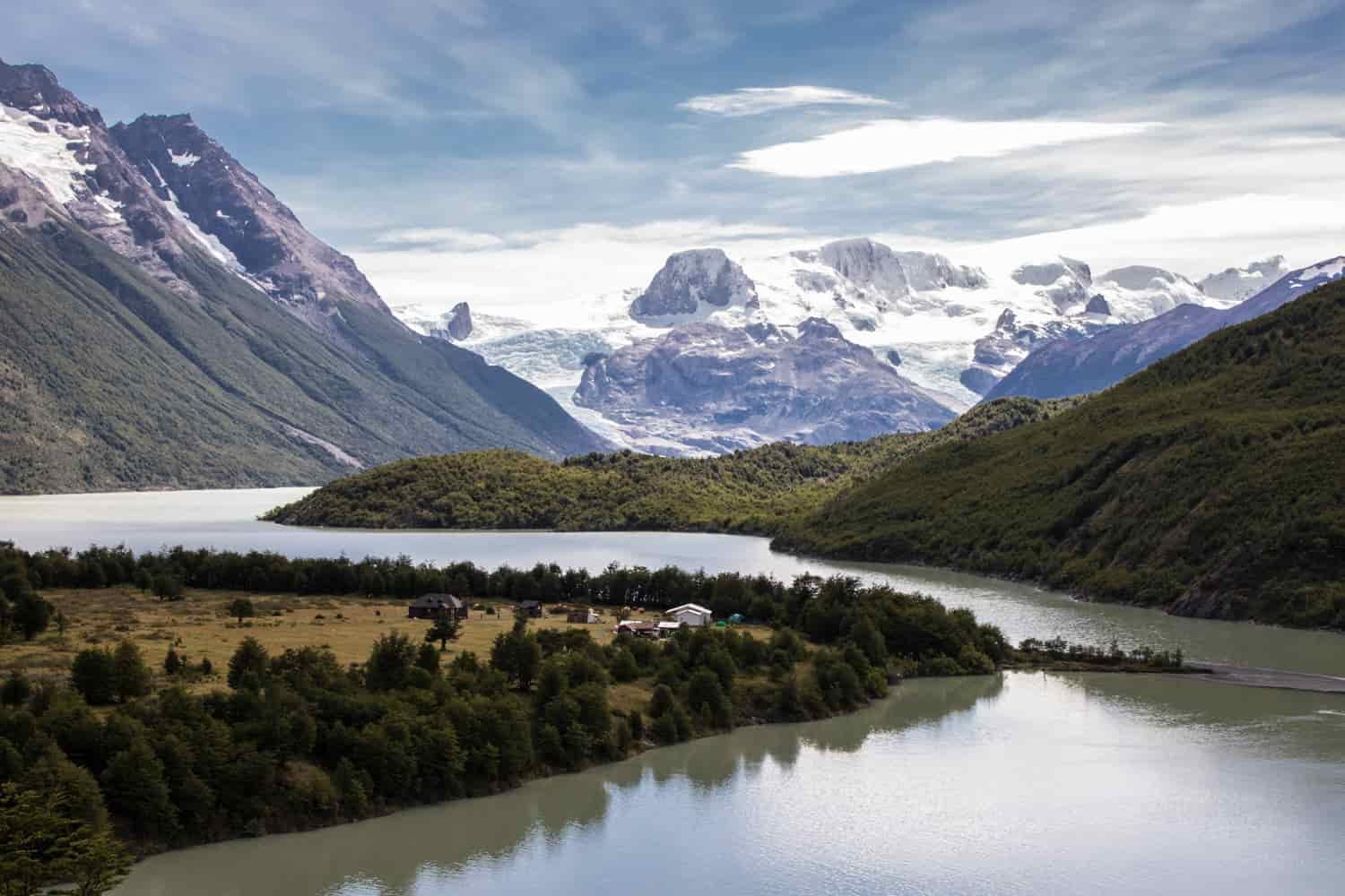 A river snakes through a valley with green and snowy mountains in the background
