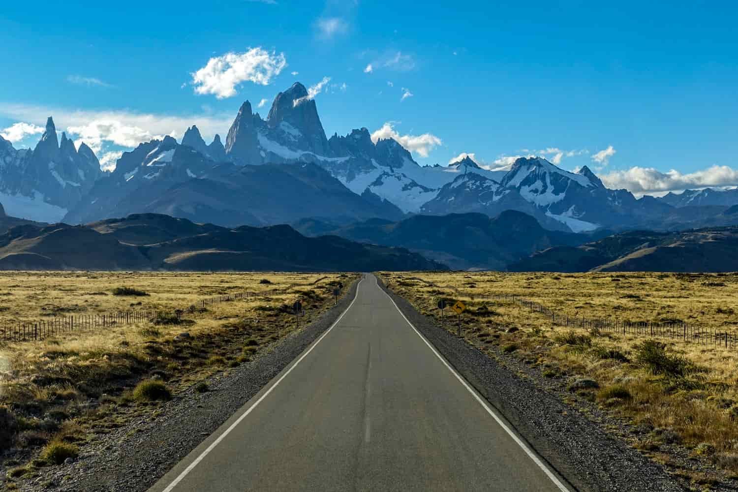 A highway heads straight toward beautiful, snow-layered mountains