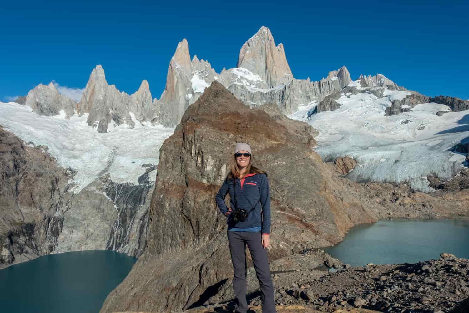 A female hiker poses on a land bridge between two mountain lakes