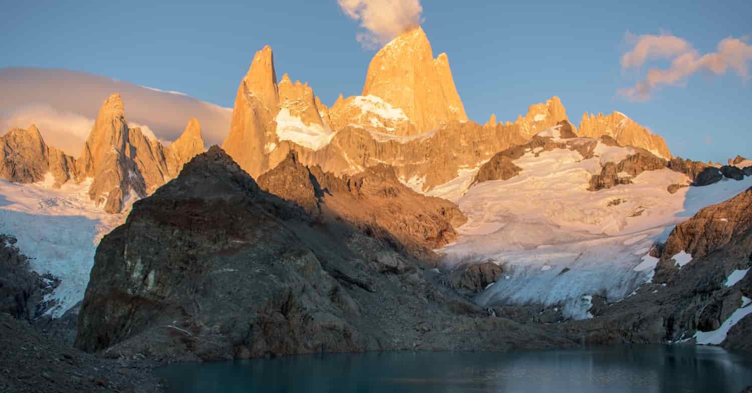 Jagged mountains are sunlit on top and shaded down low where the rock meets a mountain lake