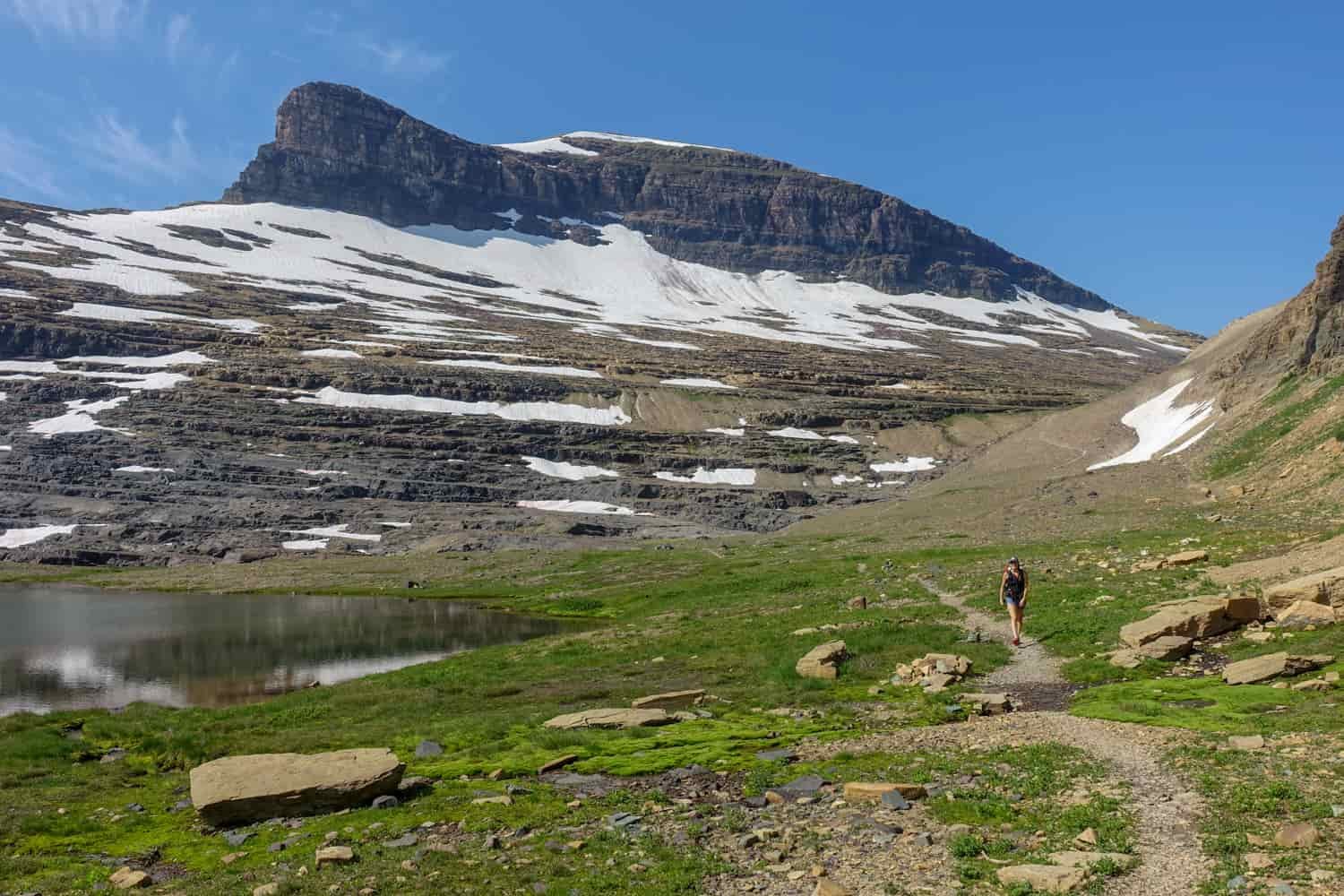 snow spotted peak above a trail with a backpacker hiking in glacier national park