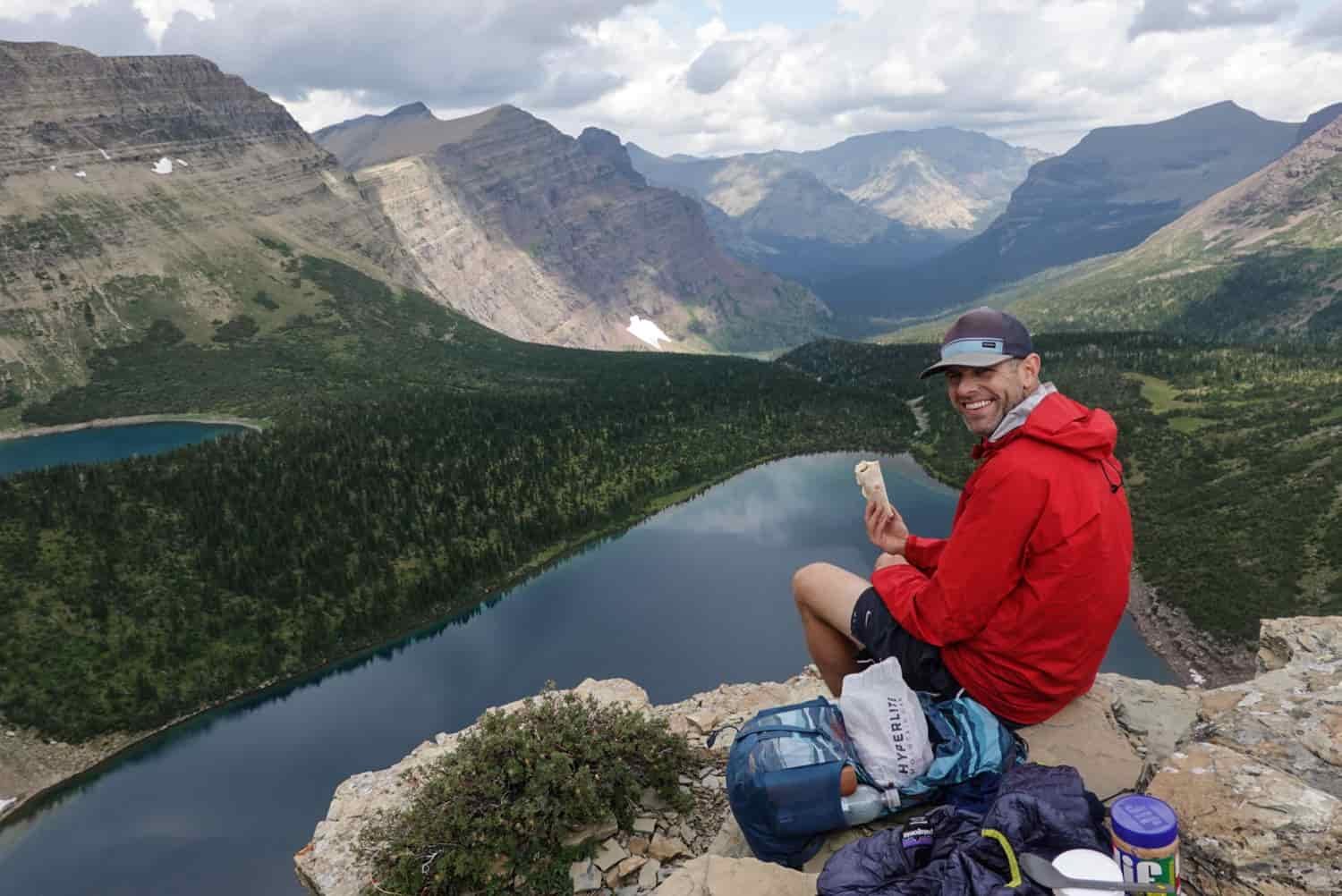 backpacker stopping for lunch on a rock ledge above a large subalpine lake in glacier national park