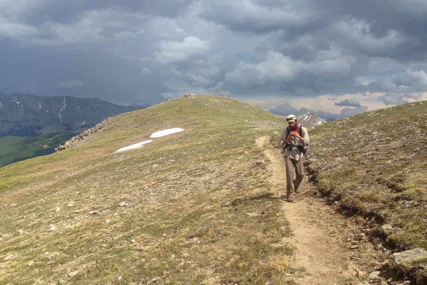 CDT thru-hiker walking away from storm clouds.