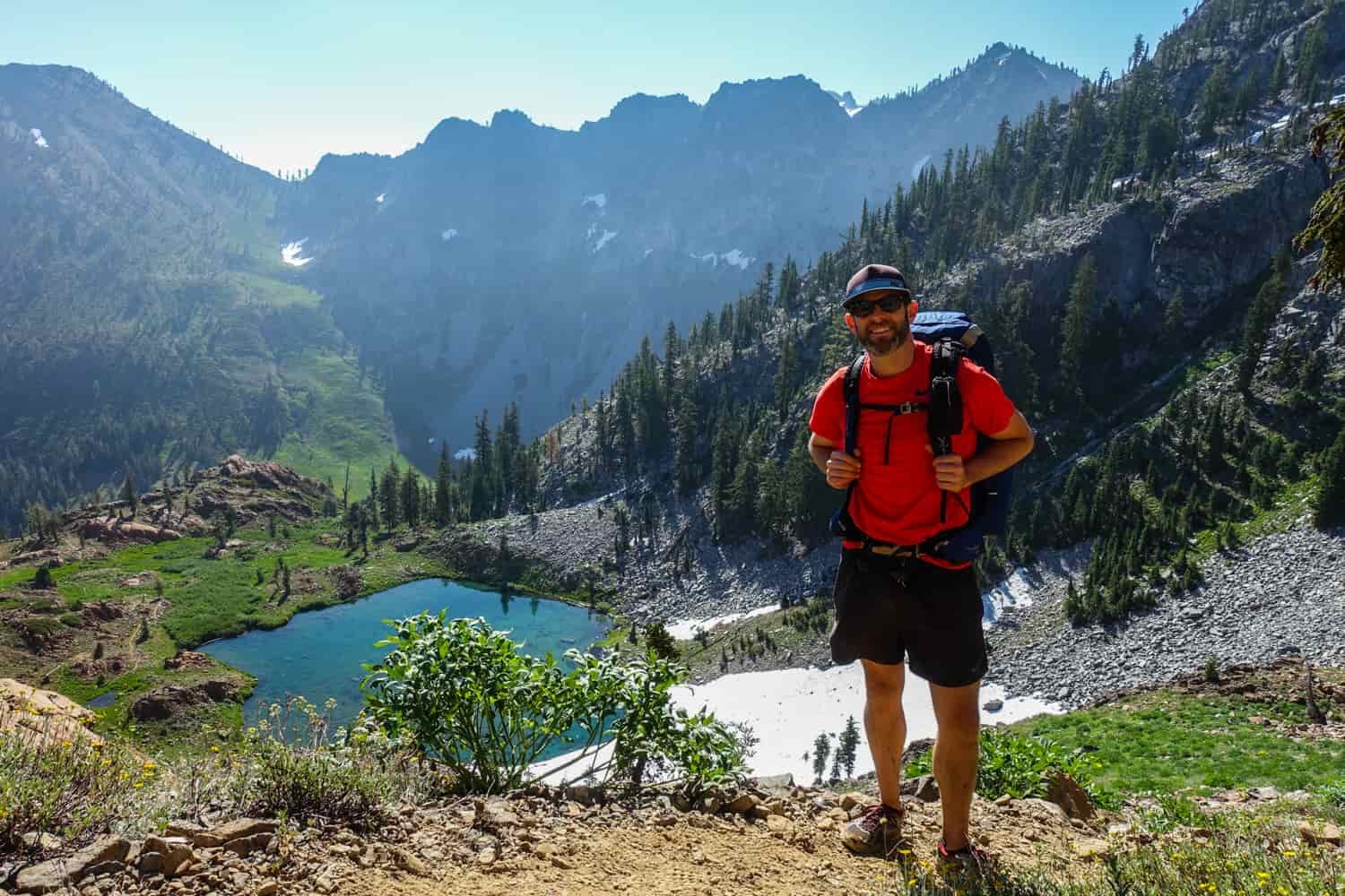 backpacker posing above a blue alpine lake snow on the north side of the lake in the trinity alps