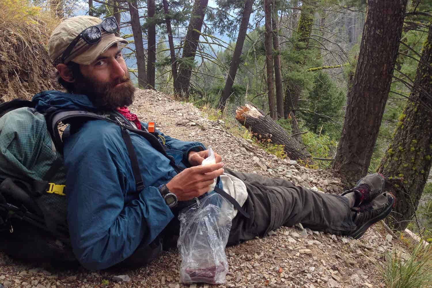 CDT thru-hiker sitting on the trail having a snack