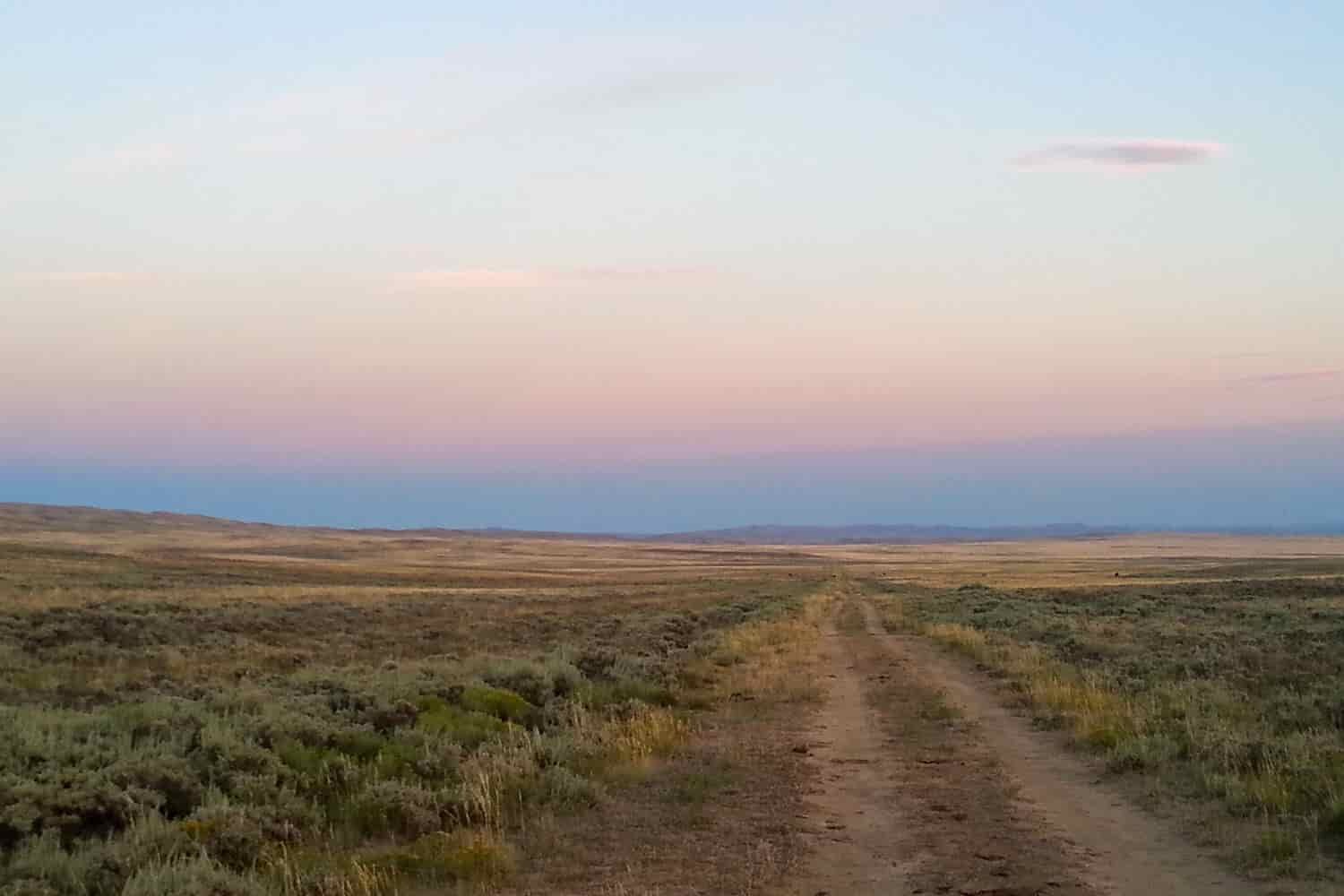 sunset across a sagebrush plain with a dirt road disappearing on the horizon.