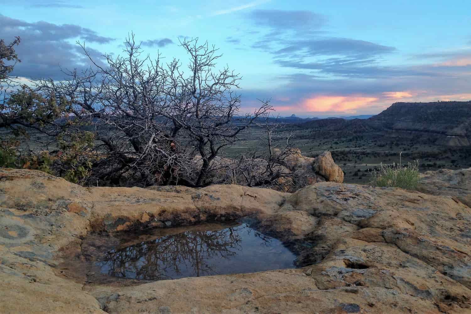 A small body of water in the desert with the sunsetting over a desert landscape