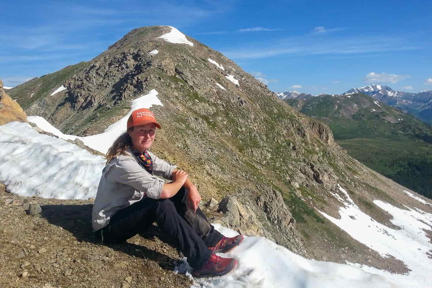 Backpacker on the CDT taking a break on a mountain ridge with snow still holding onto the mountain.