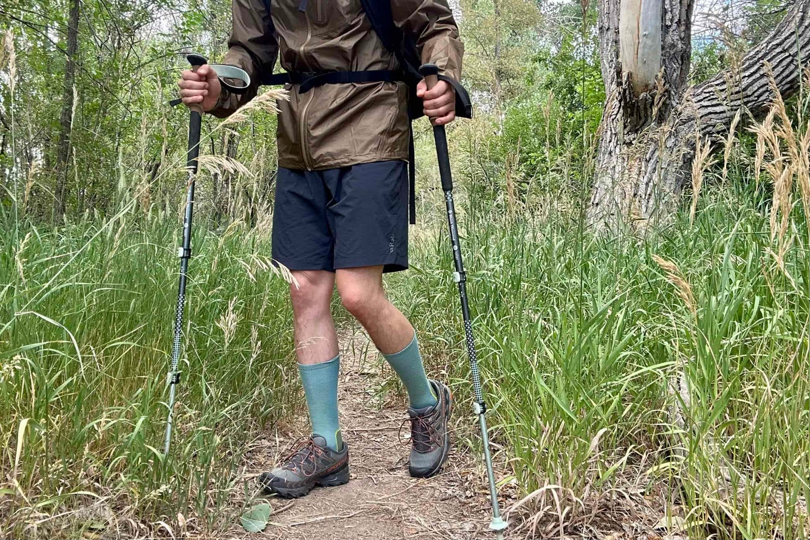 A hiker walks along a trail in a rain jacket and full backpacking gear looking off in the distance in a forest setting.