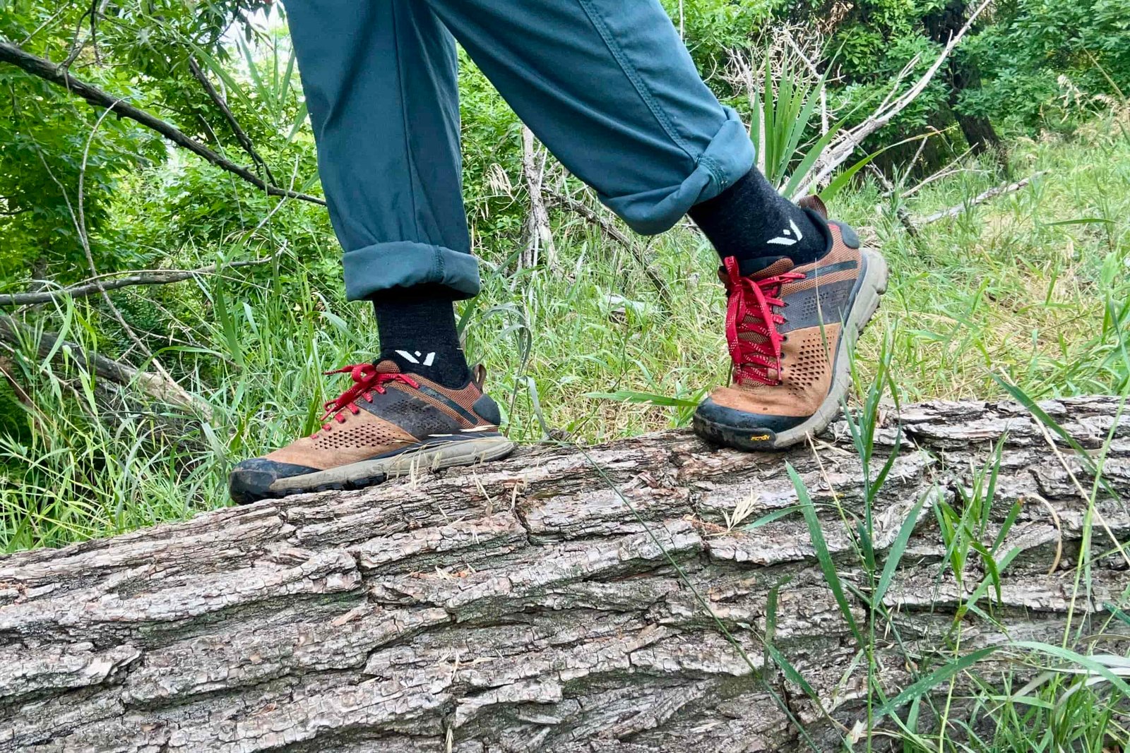 A close up shot from the knees down of a man wearing the Danner Trail 2650 hiking shoes while standing on a log.