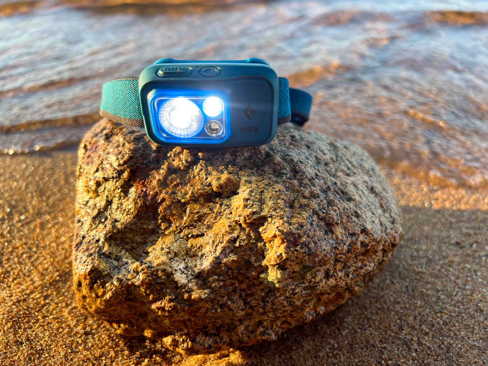 The image shows a Black Diamond Spot 400 - R sitting on a rock next to water.