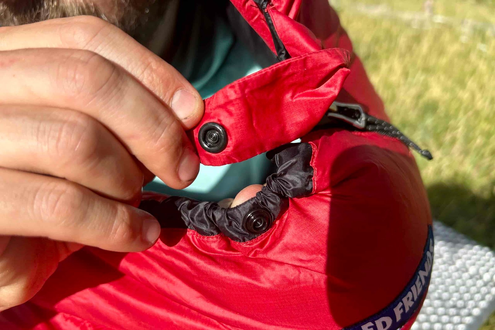 A close-up of the button closure on a sleeping bag at the top of a zipper near the hood.
