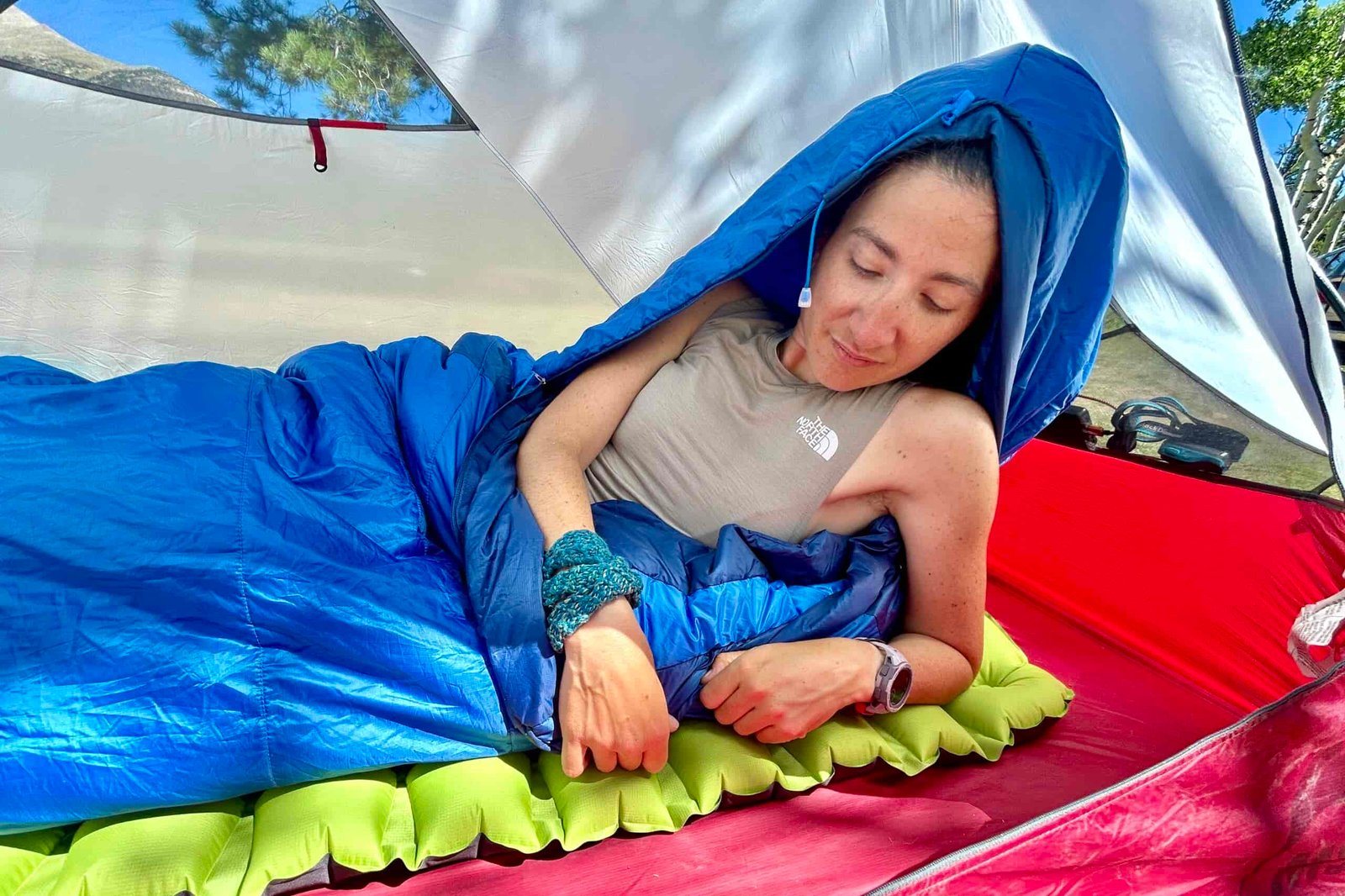 A close-up image of a woman waking up in a tent in the Marmot Trestles 20 sleeping bag in a red tent in the sun.