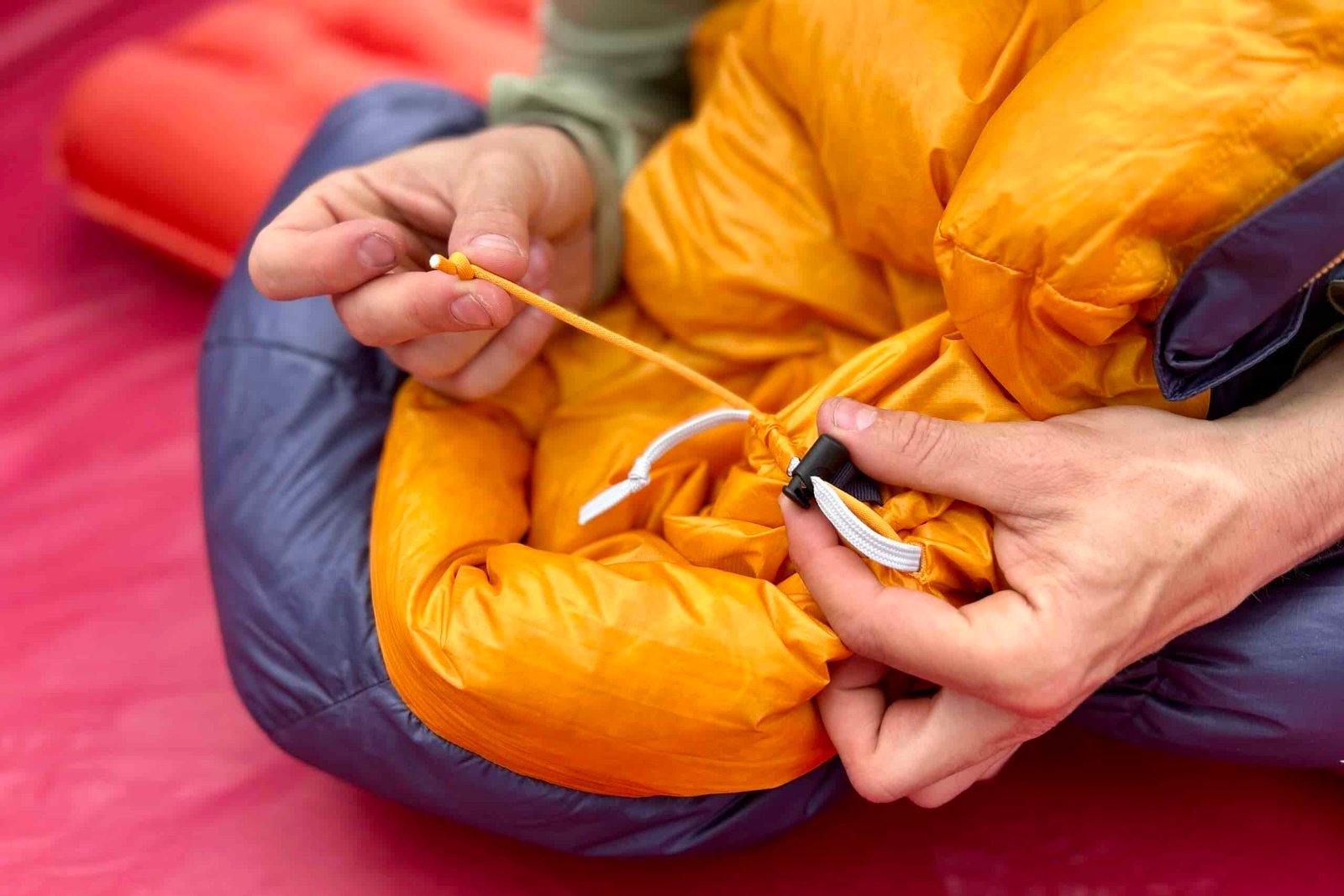 A man tightens up the cinch cord of a sleeping bag with one hand on the string, and the other holding the cinching mechanism.