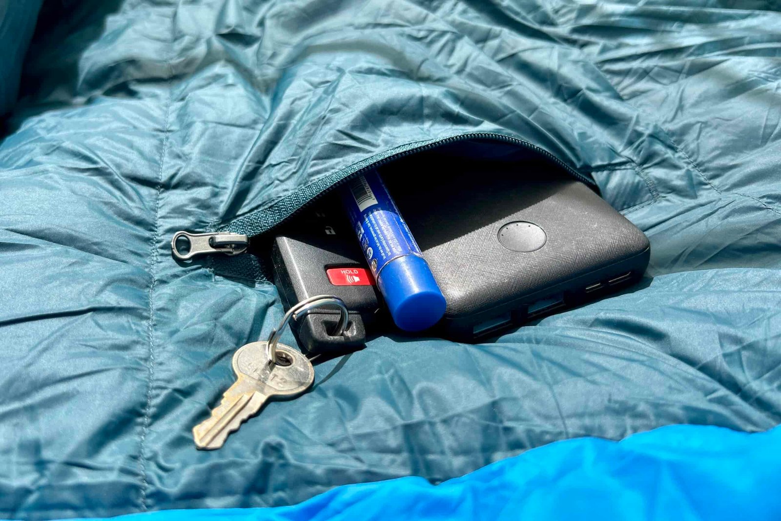 A close up image of keys, a chapstick, and a battery pack sticking out of a zippered internal sleeping bag pocket.