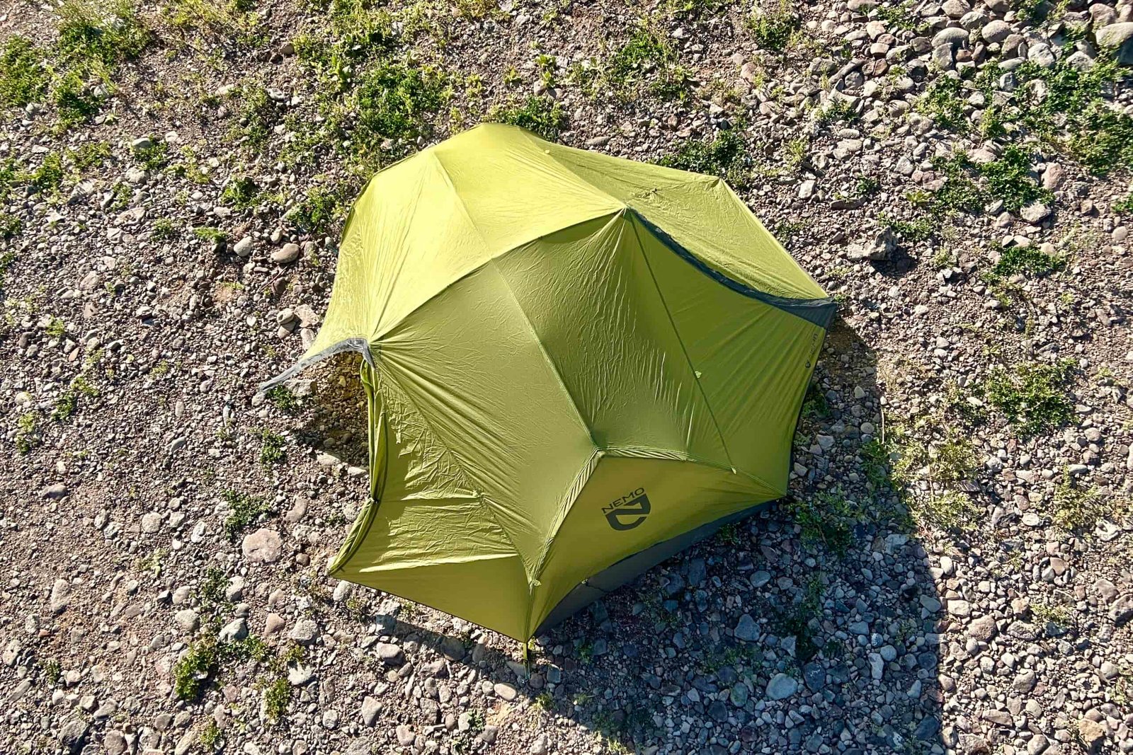 A green tent set up on rocky terrain from above.