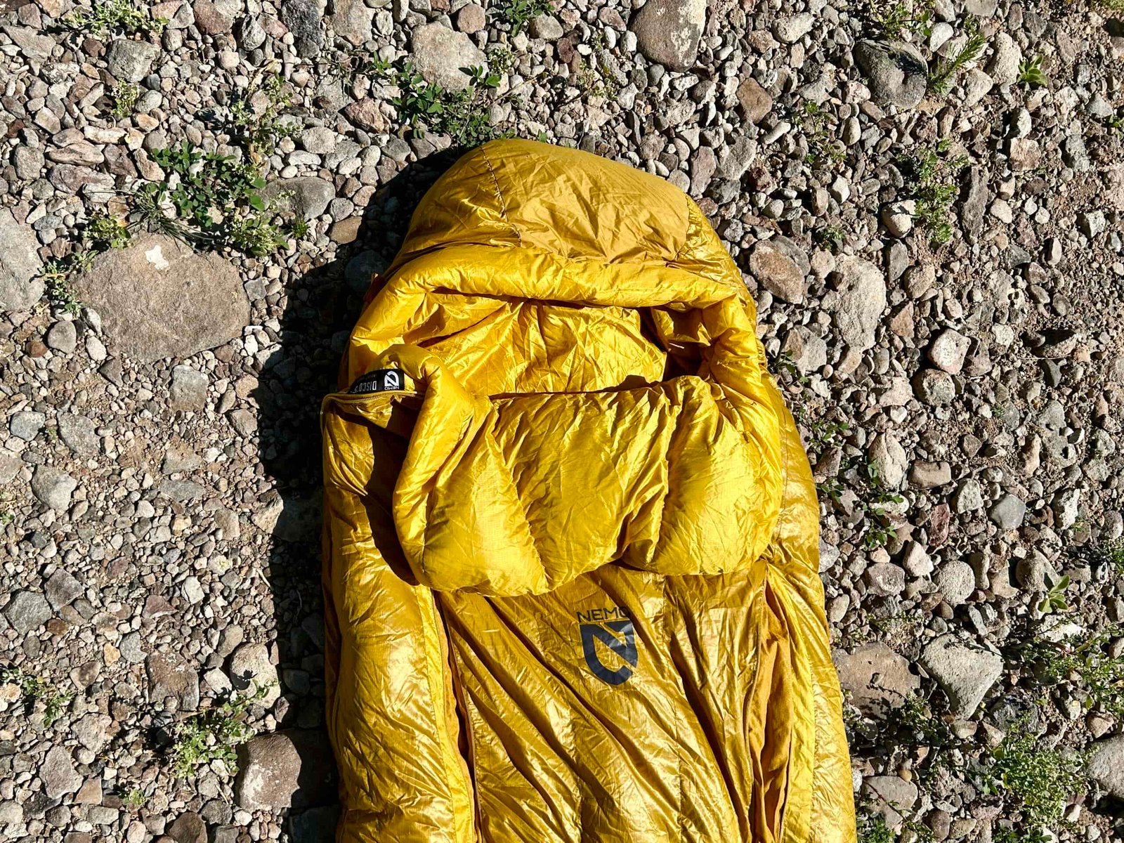 A picture from above of a sleeping bag lying on the ground. The image is from halfway up to the hood.