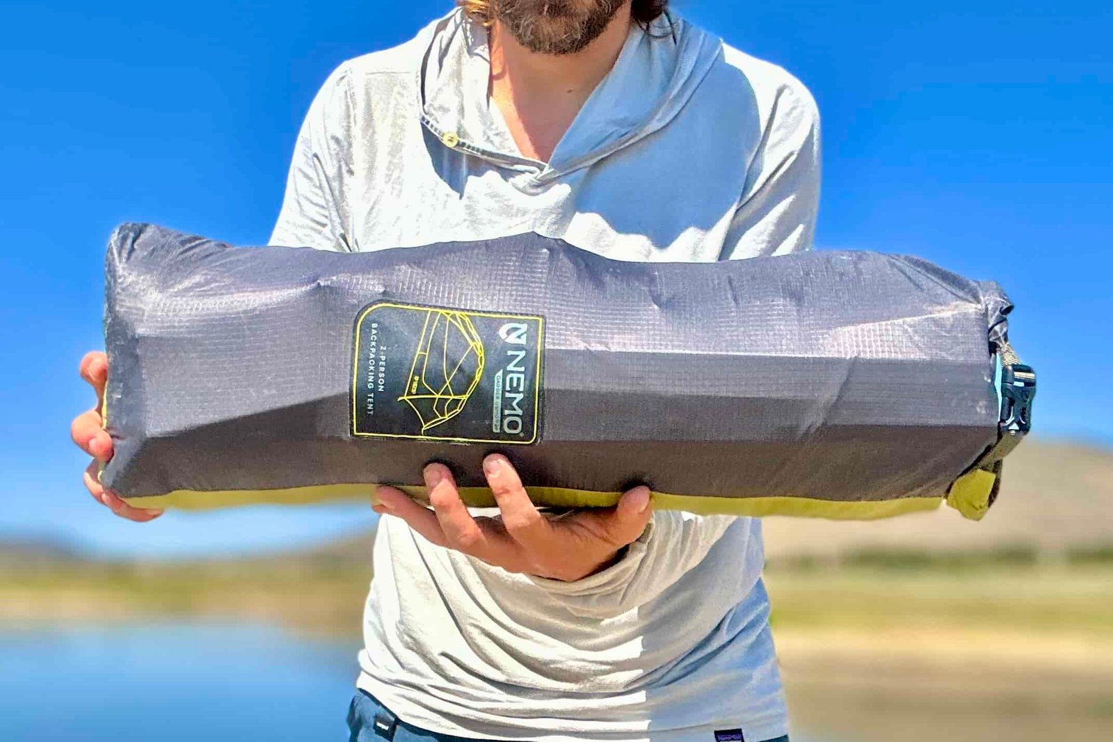 A man holds the packaged NEMO Dagger OSMO 2 with a blue sky in background.