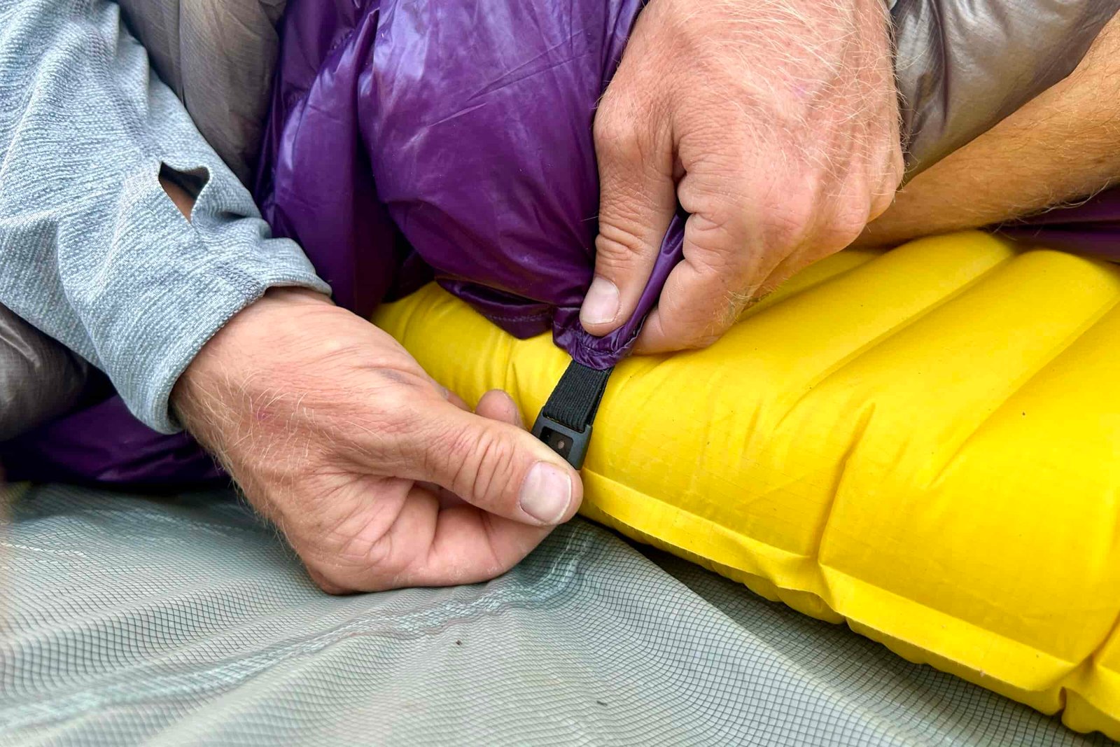 A person tightens the under-mattress attachment points of their quilt around their sleeping pad.