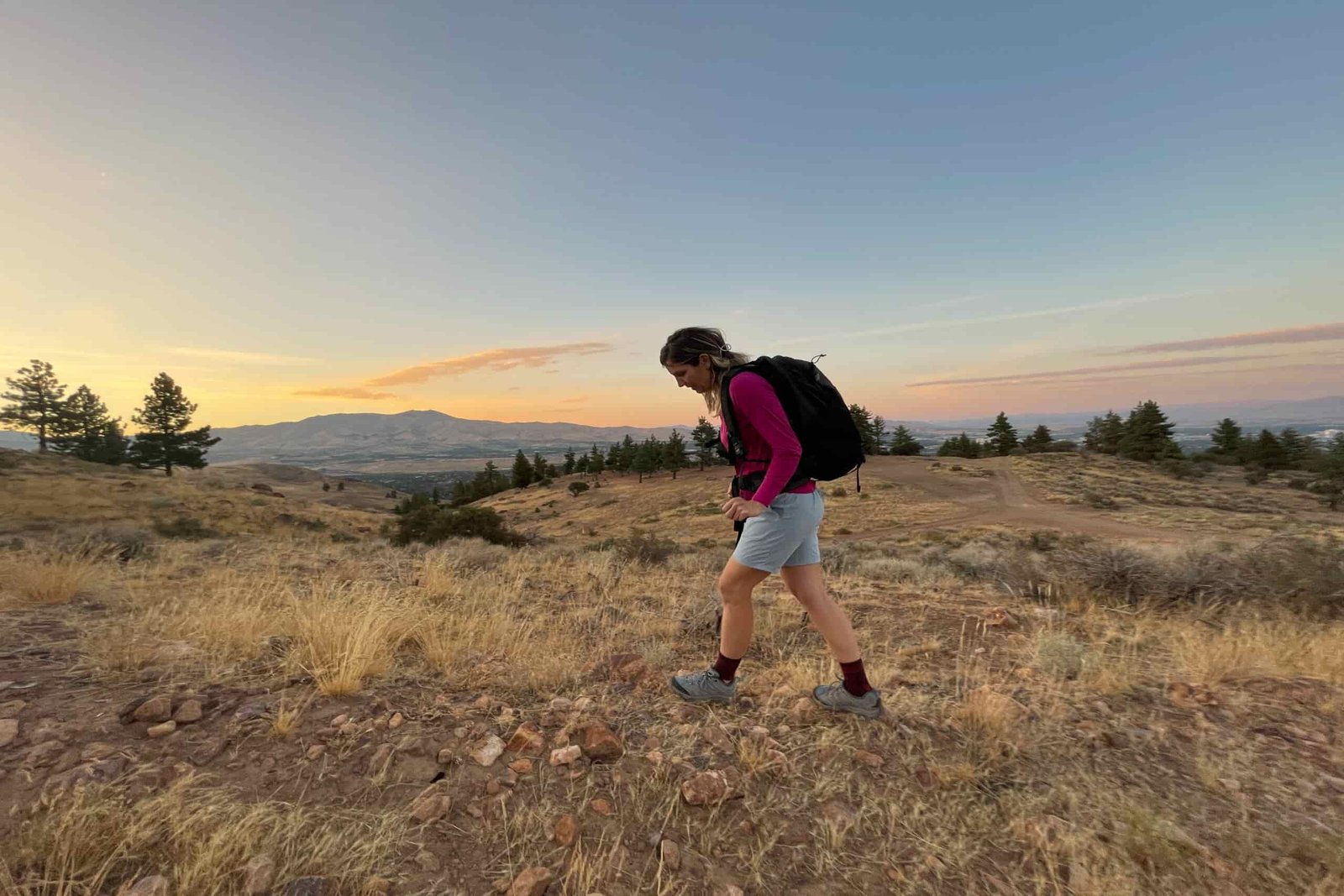 A hiker wearing houdini wadi shorts and a backpack hiking in high desert terrain at sunset