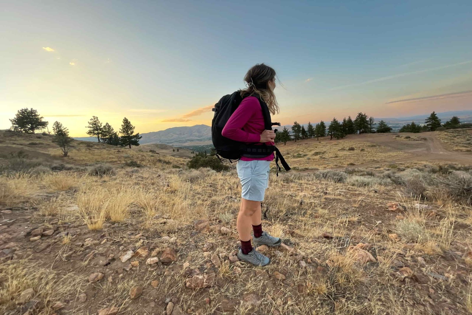 a hiker wearing a backpack and shorts watching the sunset in the mountain desert