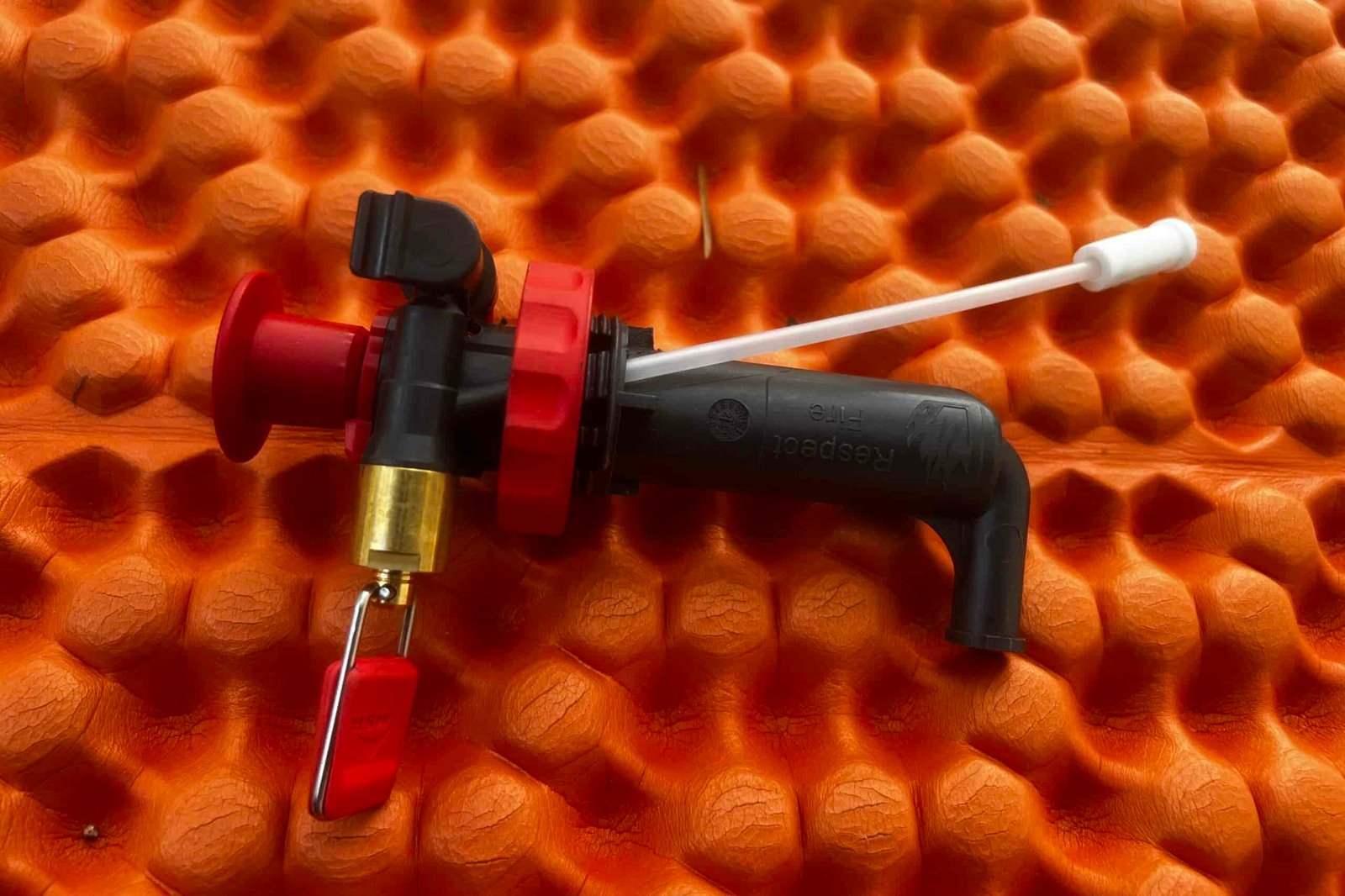 The fuel pump of the MSR Whisperlite sitting on an orange, foam sleeping mat.