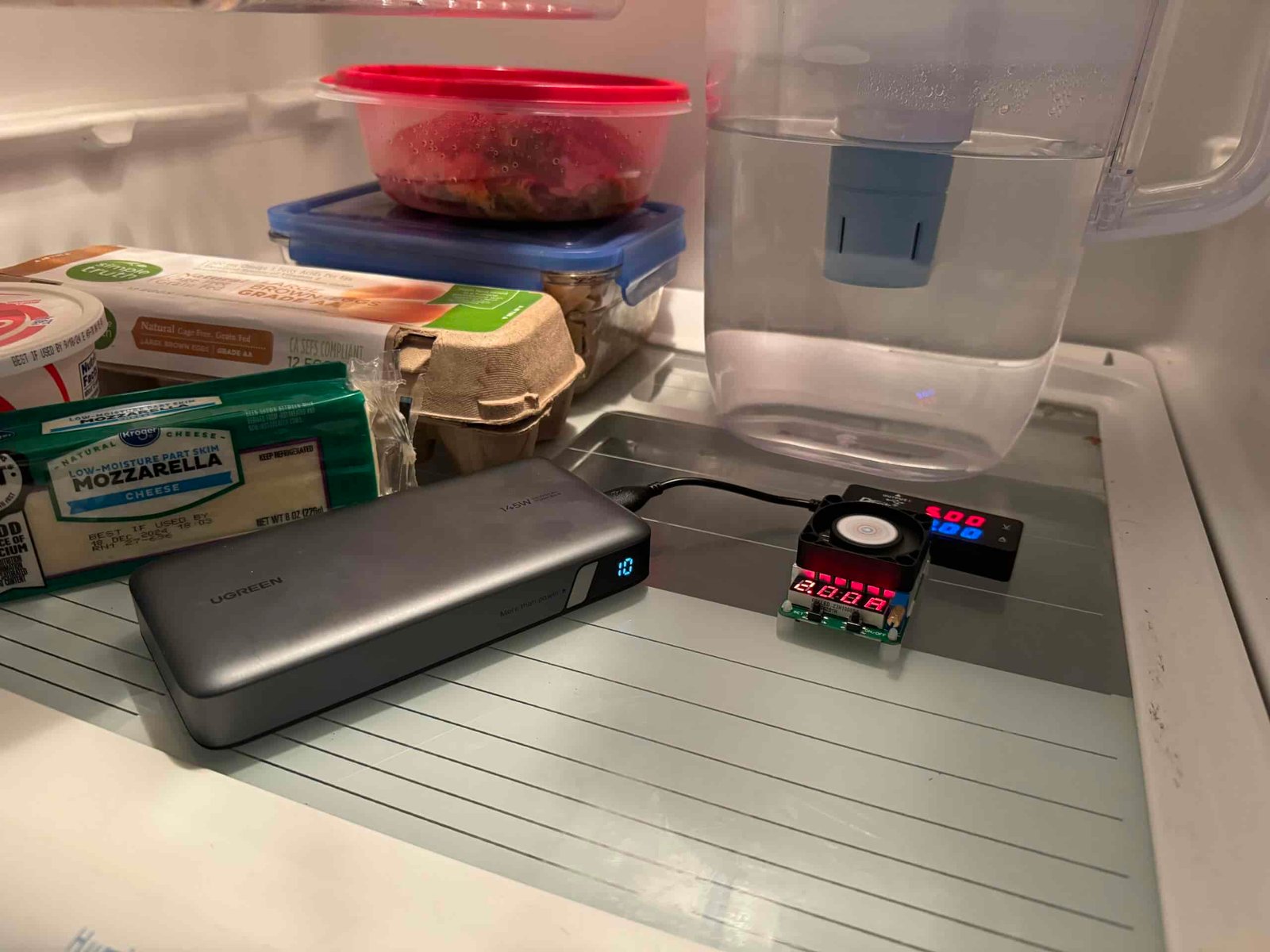 The UGREEN power bank is hooked up to a multimeter and dummy resistor load inside a refrigerator with food.