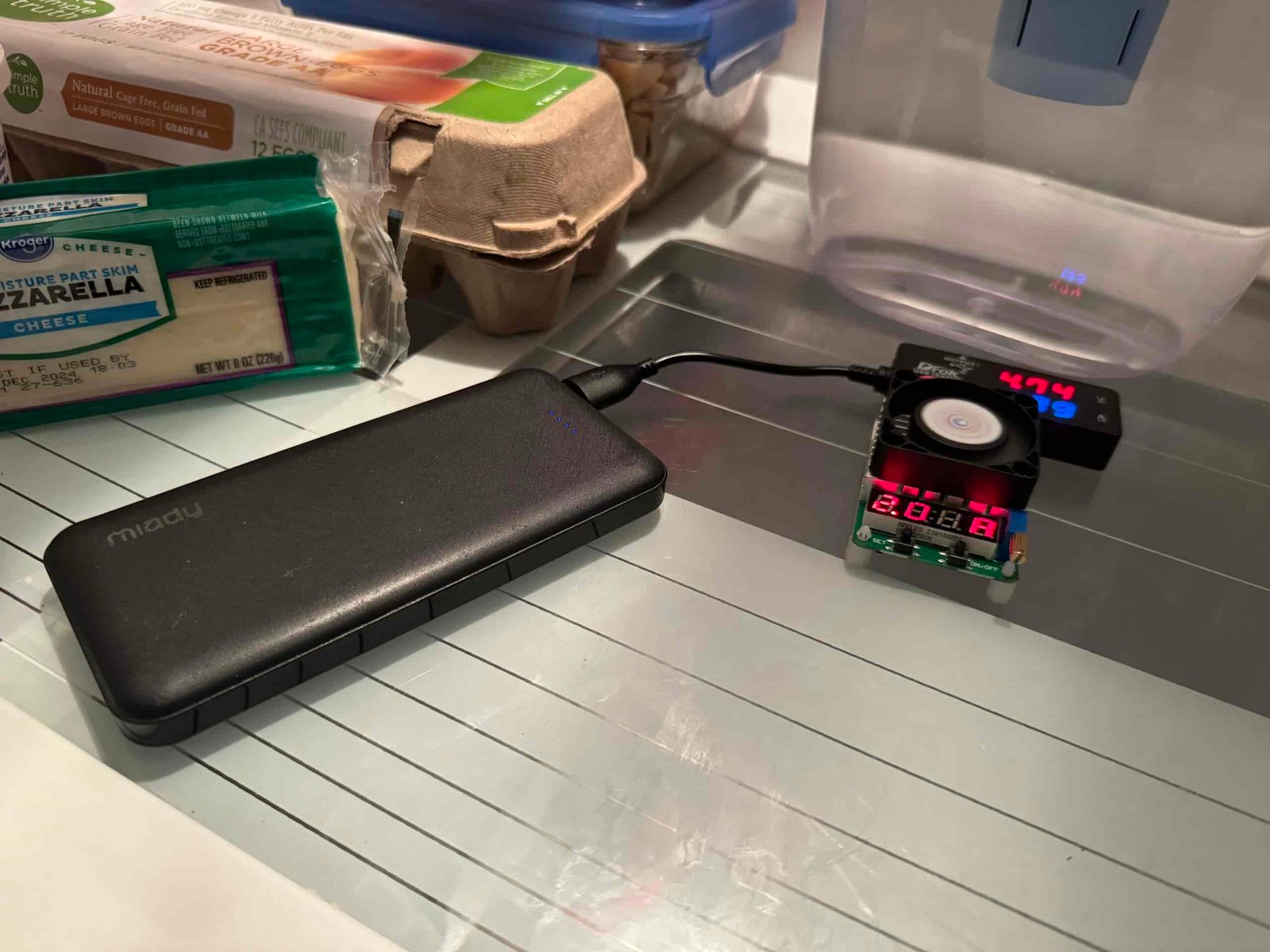 The Miady power bank is hooked up to a multimeter and dummy resistor load inside a refrigerator with food.
